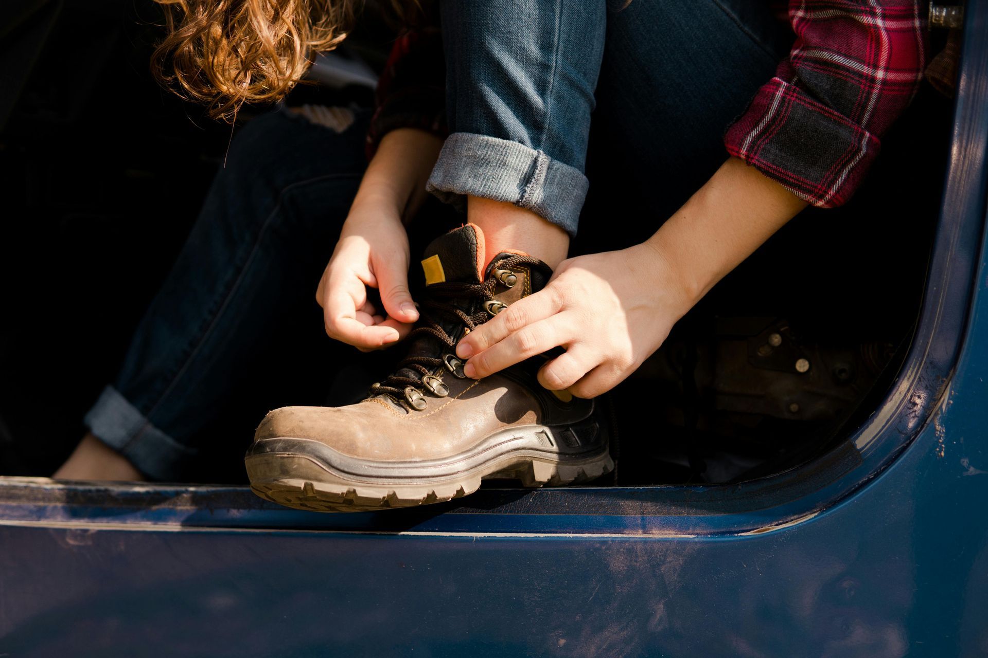 A person is sitting in the back of a truck tying their boots.