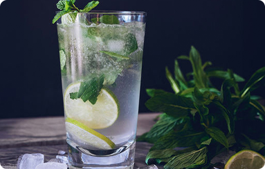 A glass of water with ice , lime slices and mint leaves on a table.