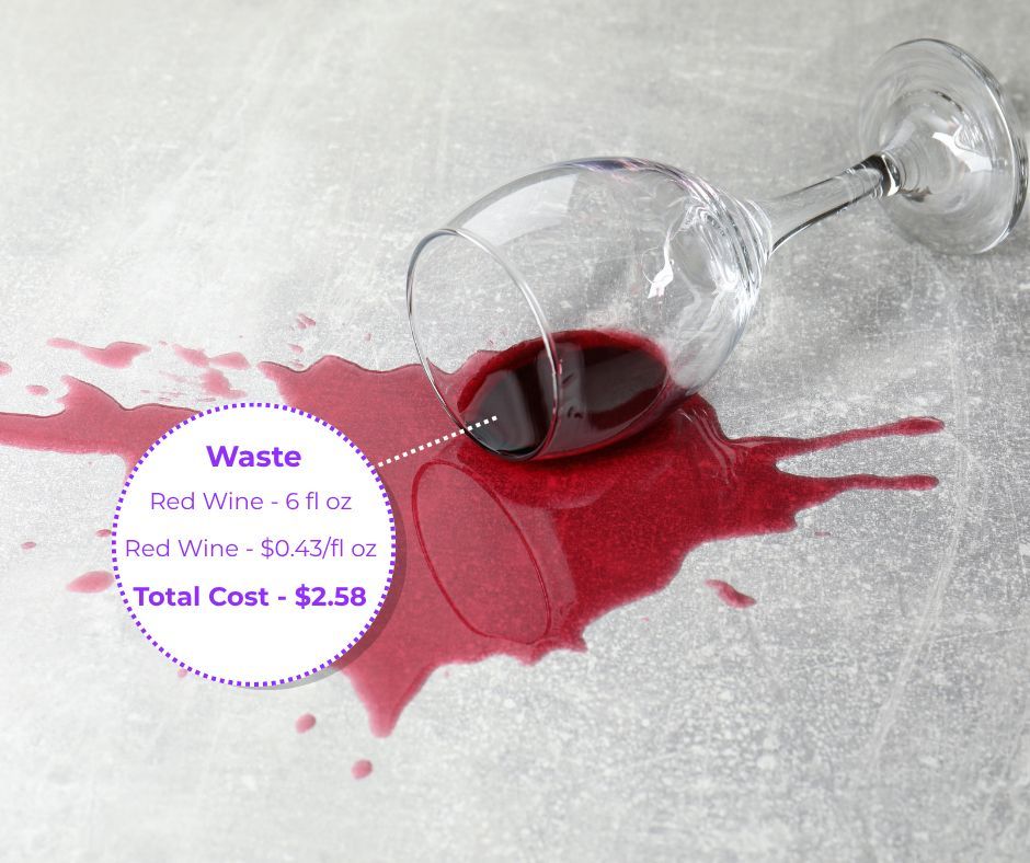 A glass of red wine with pink petals on top is on a table.