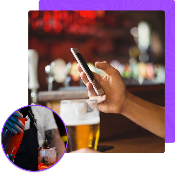 A person holding a cell phone next to a glass of beer