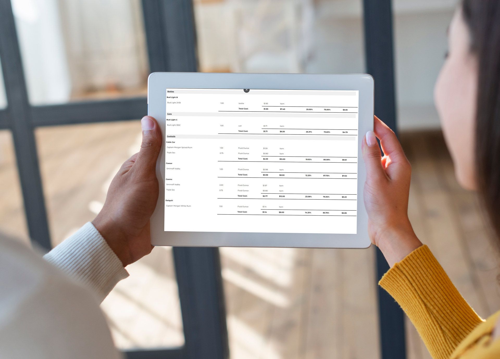 A woman is holding a tablet with a spreadsheet on it.
