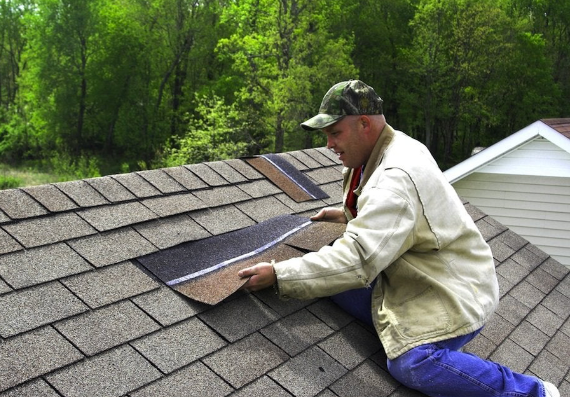 A man is kneeling on top of a roof working on it.