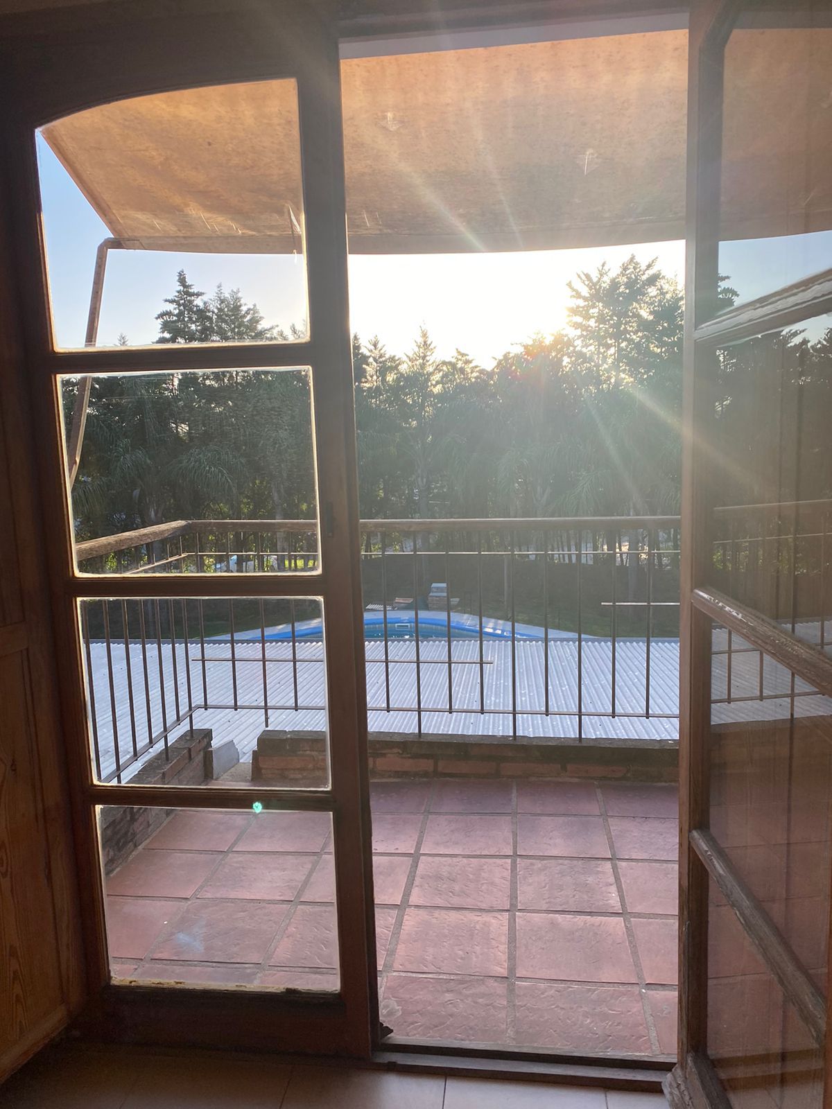 View through a doorway onto a balcony with a pool, trees, and sunlight.