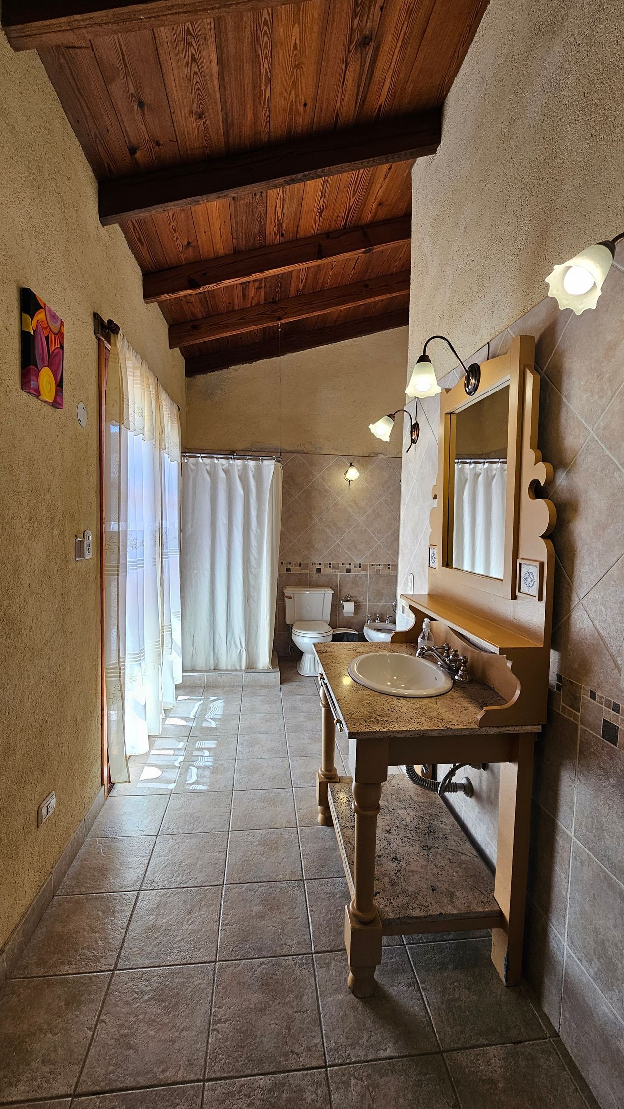 Bathroom with wood beam ceiling, vanity with mirror, toilet, shower, and stone floor.