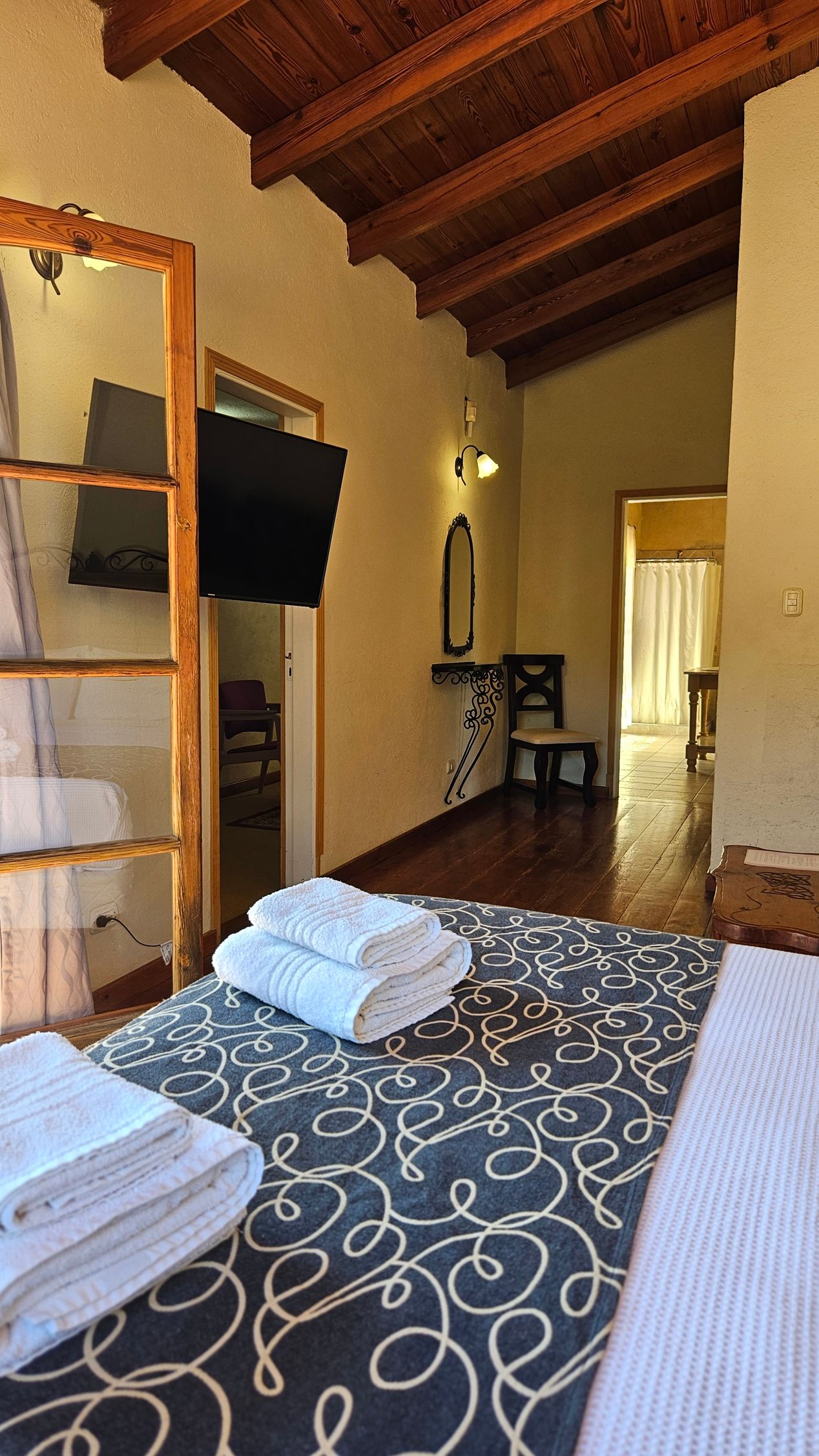 Bedroom interior with a bed, towels, TV, and exposed wood beam ceiling.
