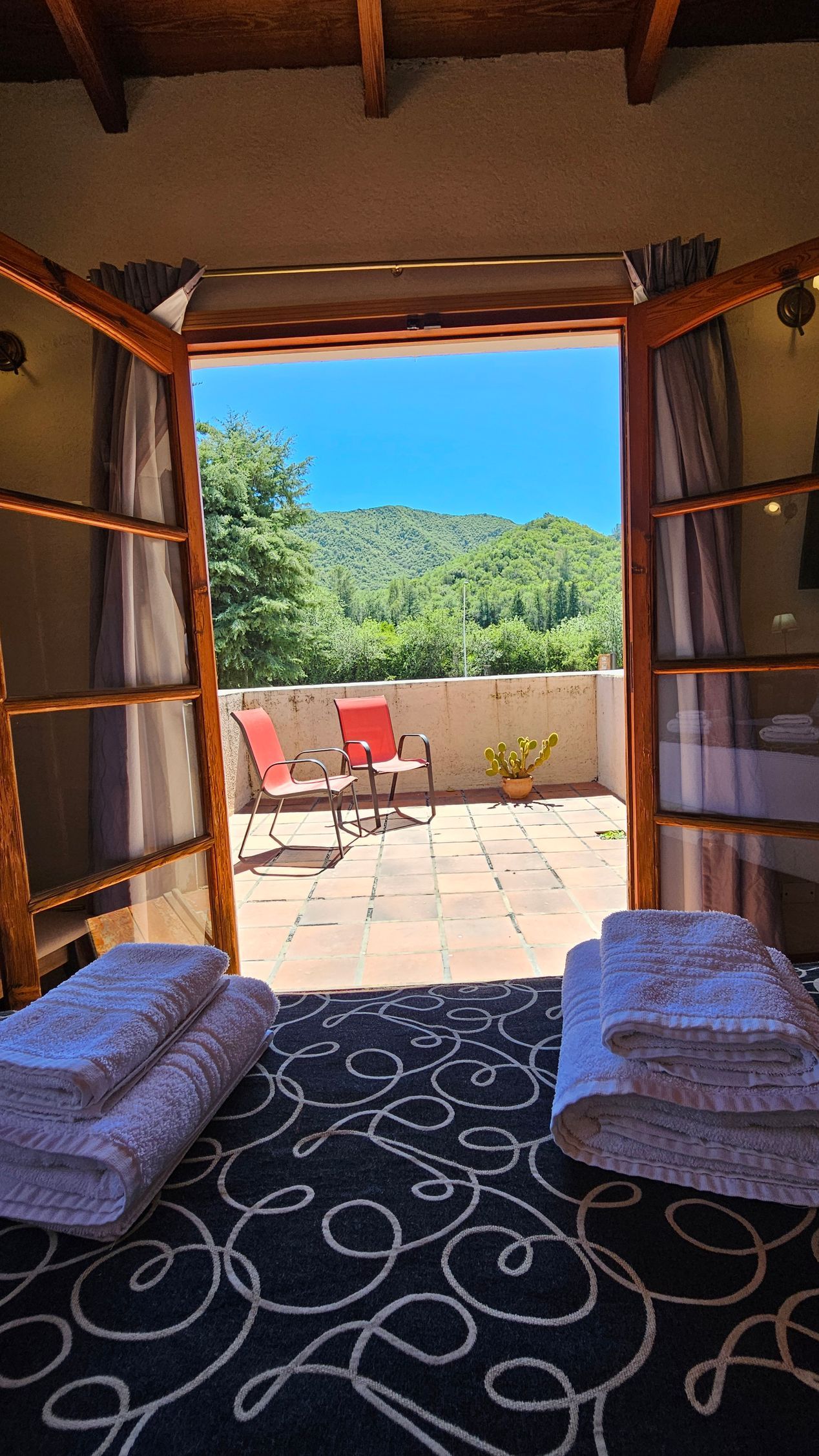 Open doors lead to a terrace with two red chairs facing a forested hillside.