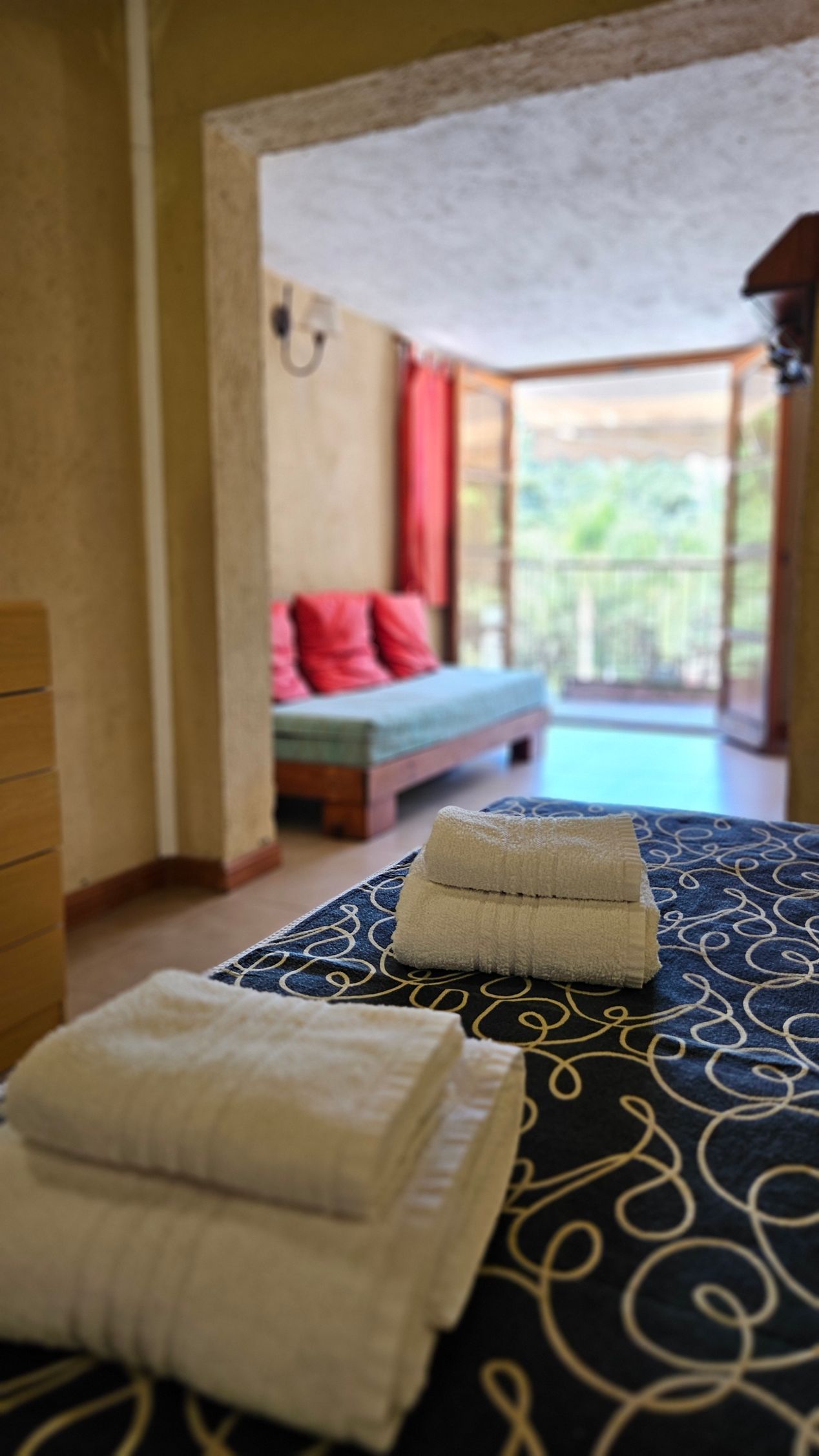 Bedroom with neatly stacked white towels on a bed; a second bed visible through a doorway.