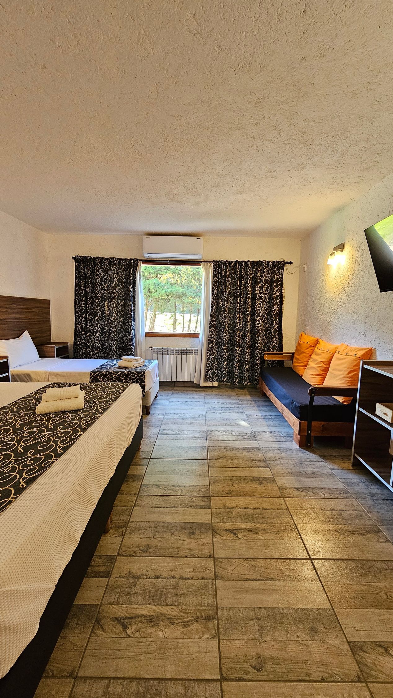 Cozy studio apartment with a bed, sofa, patterned curtains, and a stone-tiled floor.