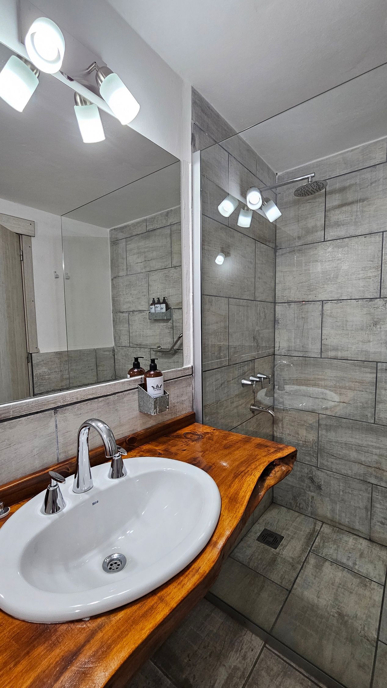 Bathroom with wood countertop, white sink, large mirror, and glass shower enclosure.