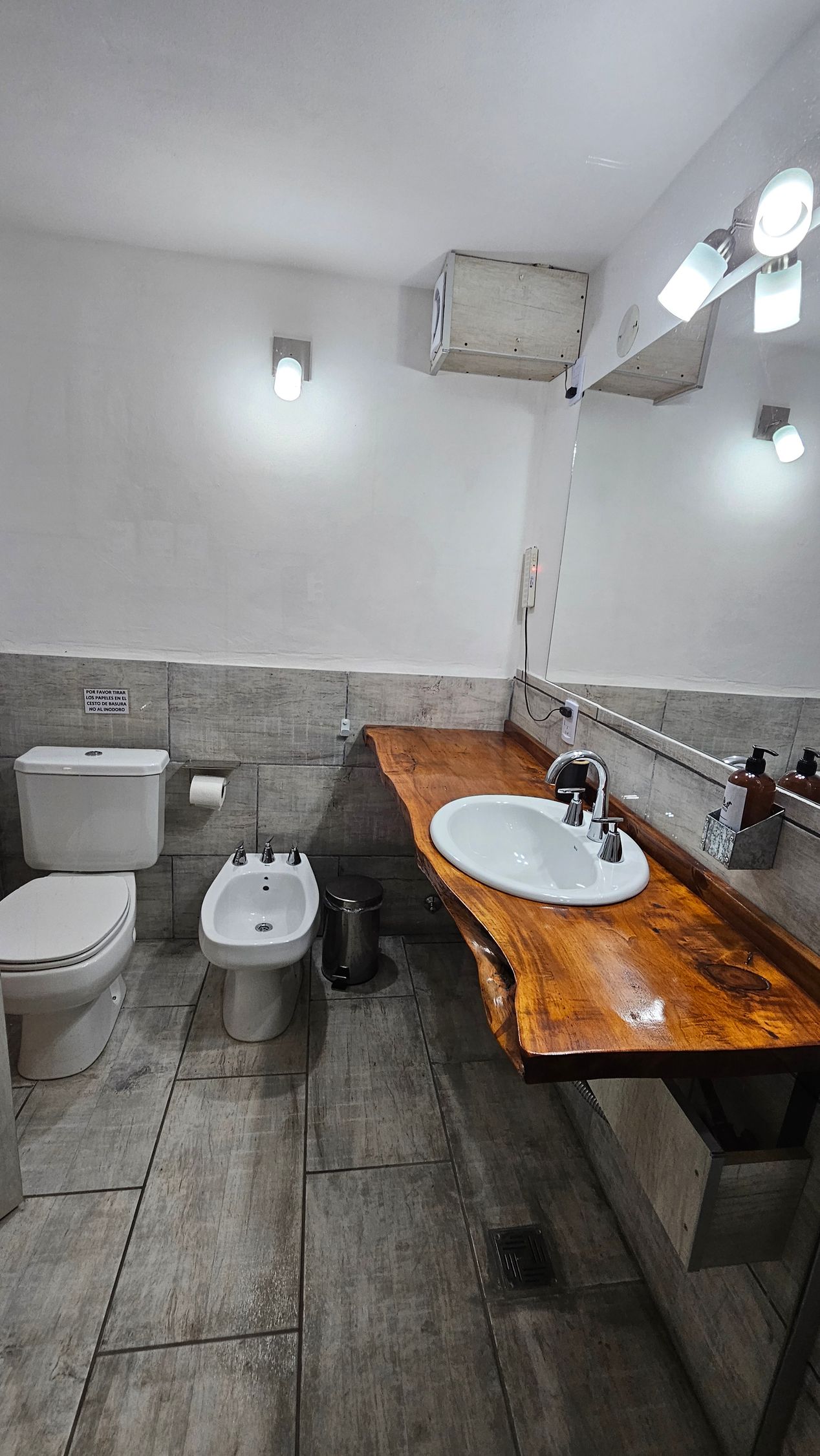 Bathroom with a wooden counter, white sink, toilet, bidet, and gray tile flooring and wall accents.
