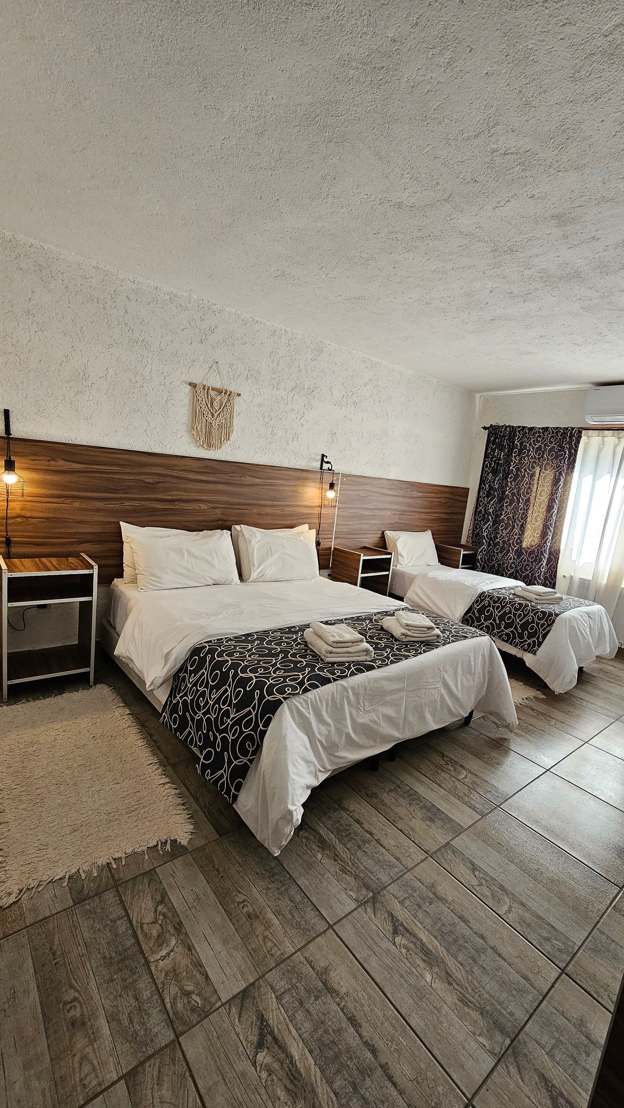 Bedroom with two beds, wood headboard, patterned bedding, and textured white ceiling and walls.