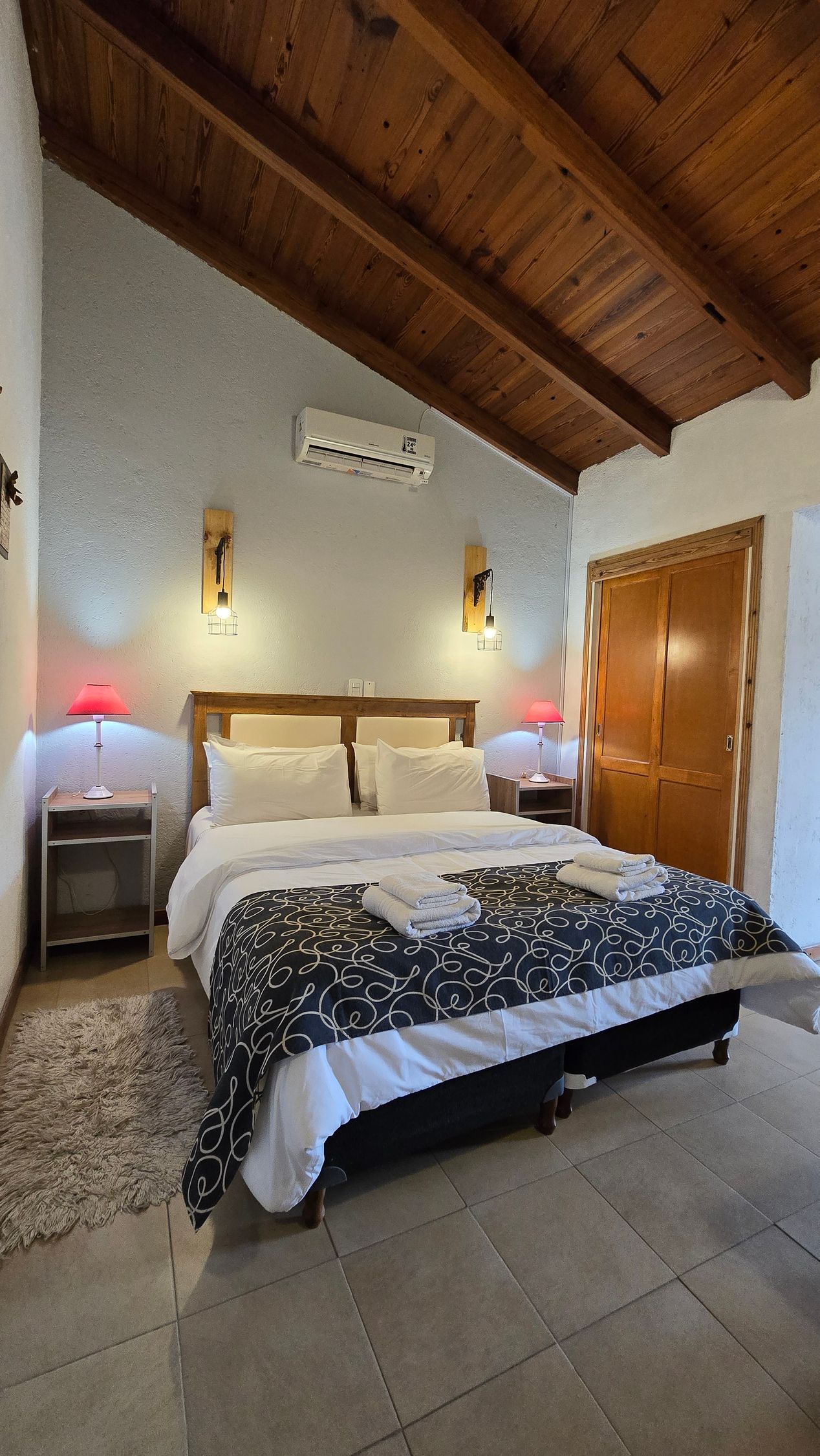 Bedroom with wooden beam ceiling, bed with black and white patterned comforter, and nightstands.
