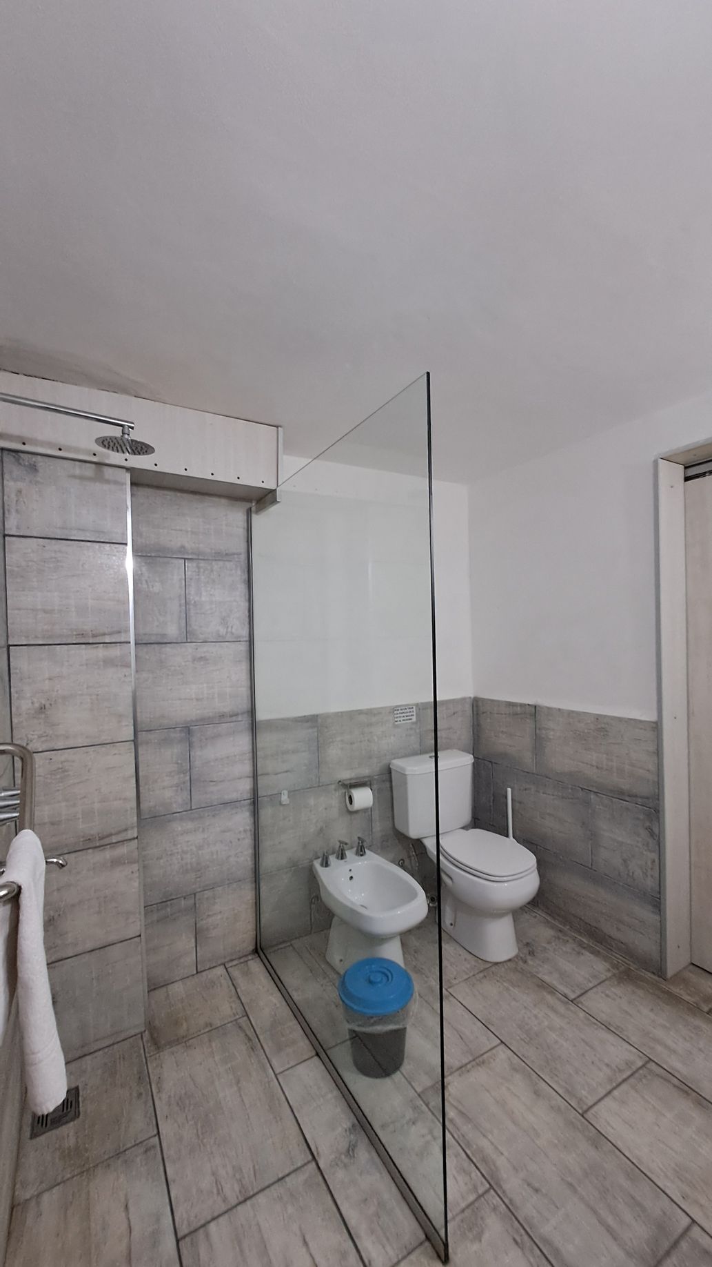 Bathroom with tiled shower, toilet, and bidet. Glass shower screen. White walls. Gray and white tiles.