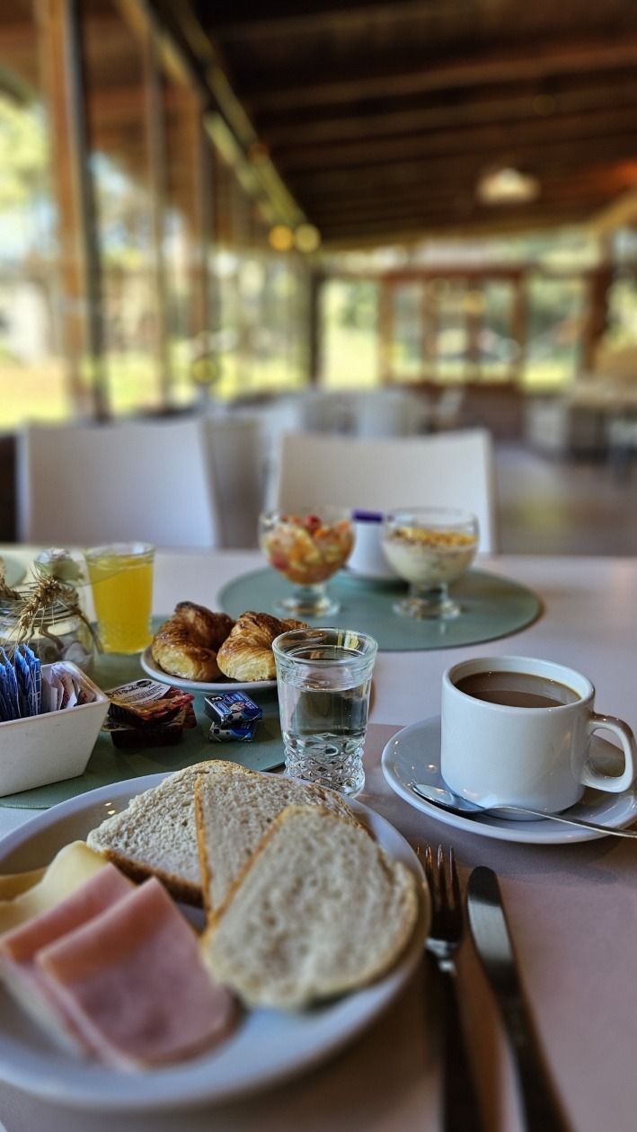 Breakfast table set with bread, ham, cheese, pastries, coffee, juice, and fruit.