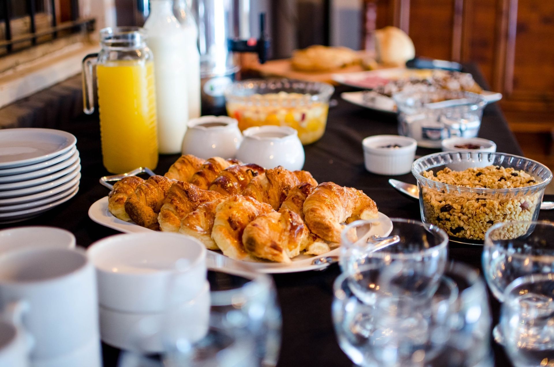 Breakfast buffet with croissants, juice, granola, and dishes on a table.