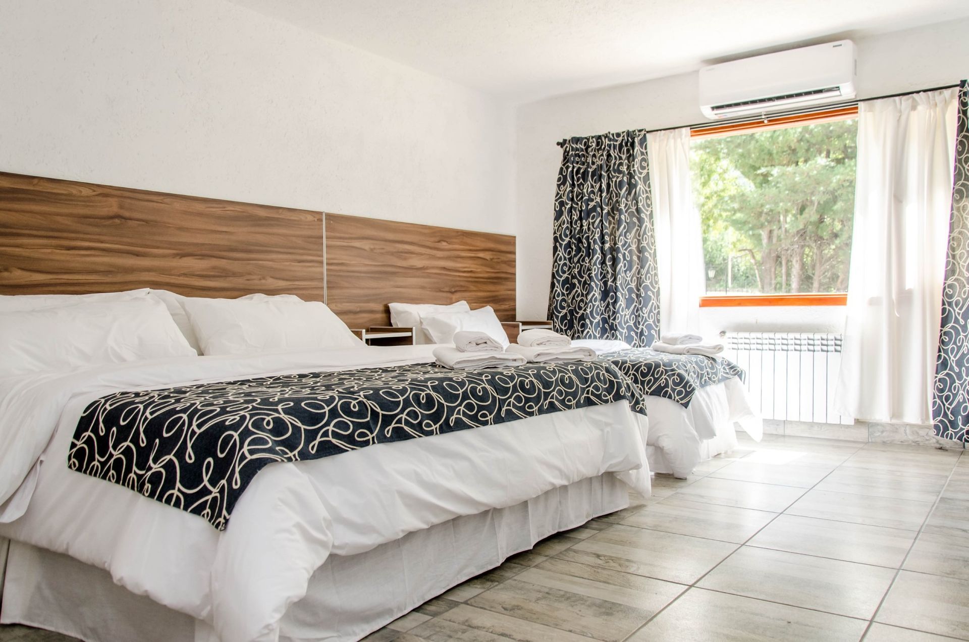 Hotel room with two beds, white bedding, floral runner, large window with view.