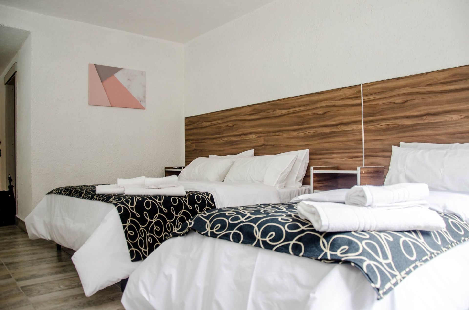 Hotel room with two double beds, white bedding, decorative bed runners, and artwork.