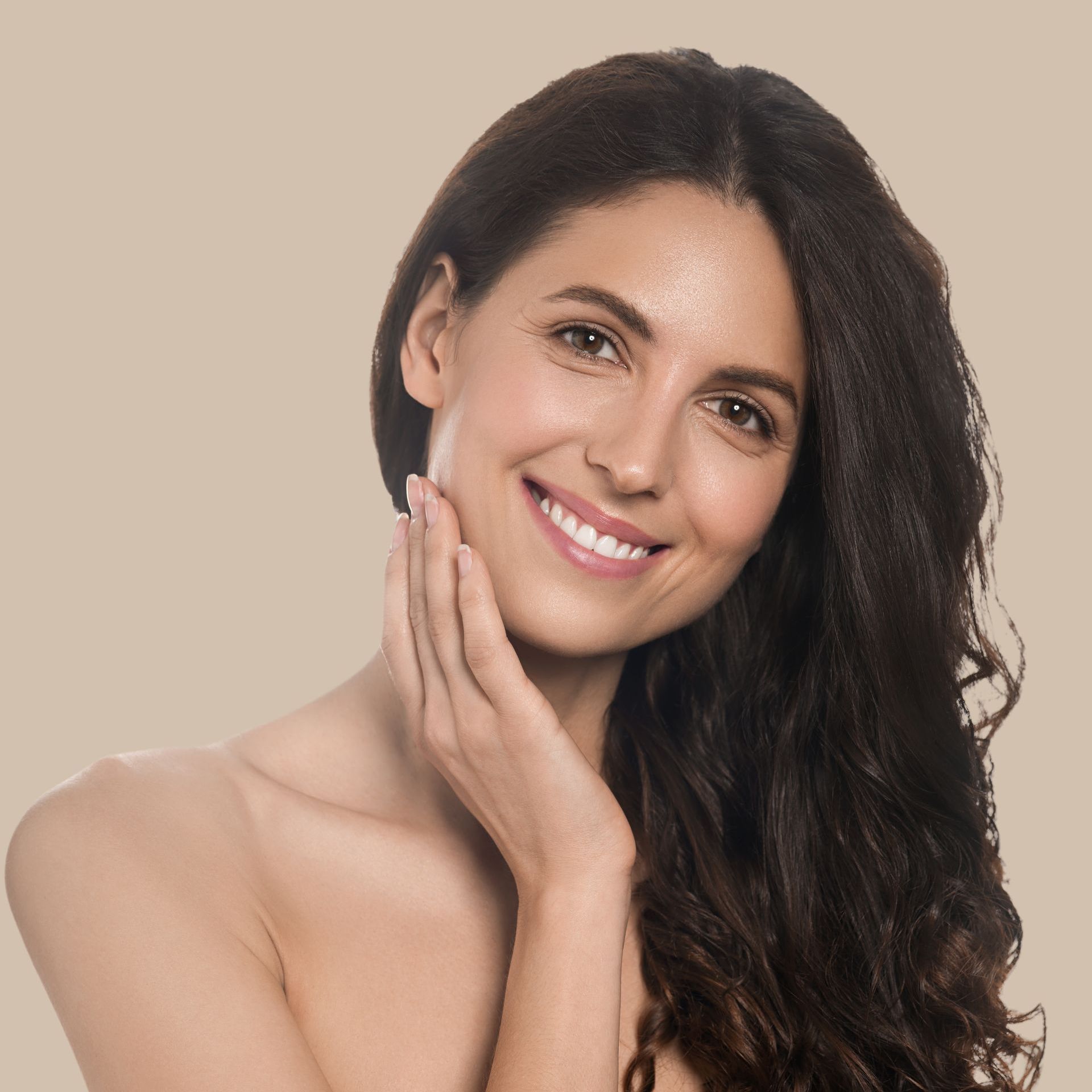 A woman with long hair is smiling and touching her face.