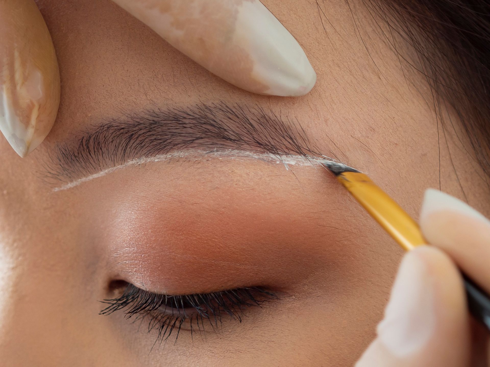 A woman is getting her eyebrows painted with a brush.