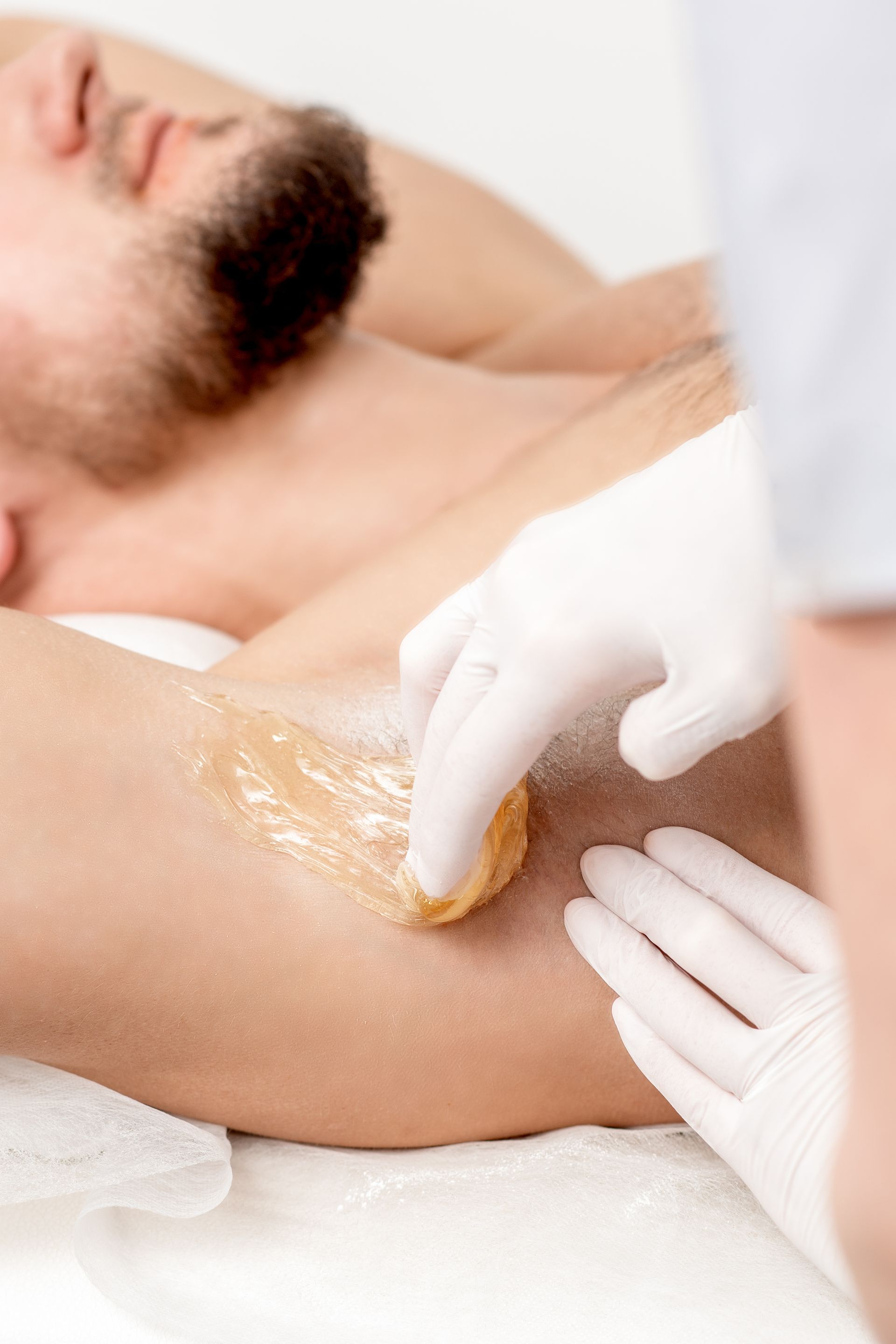 A man is getting his armpit waxed by a woman.