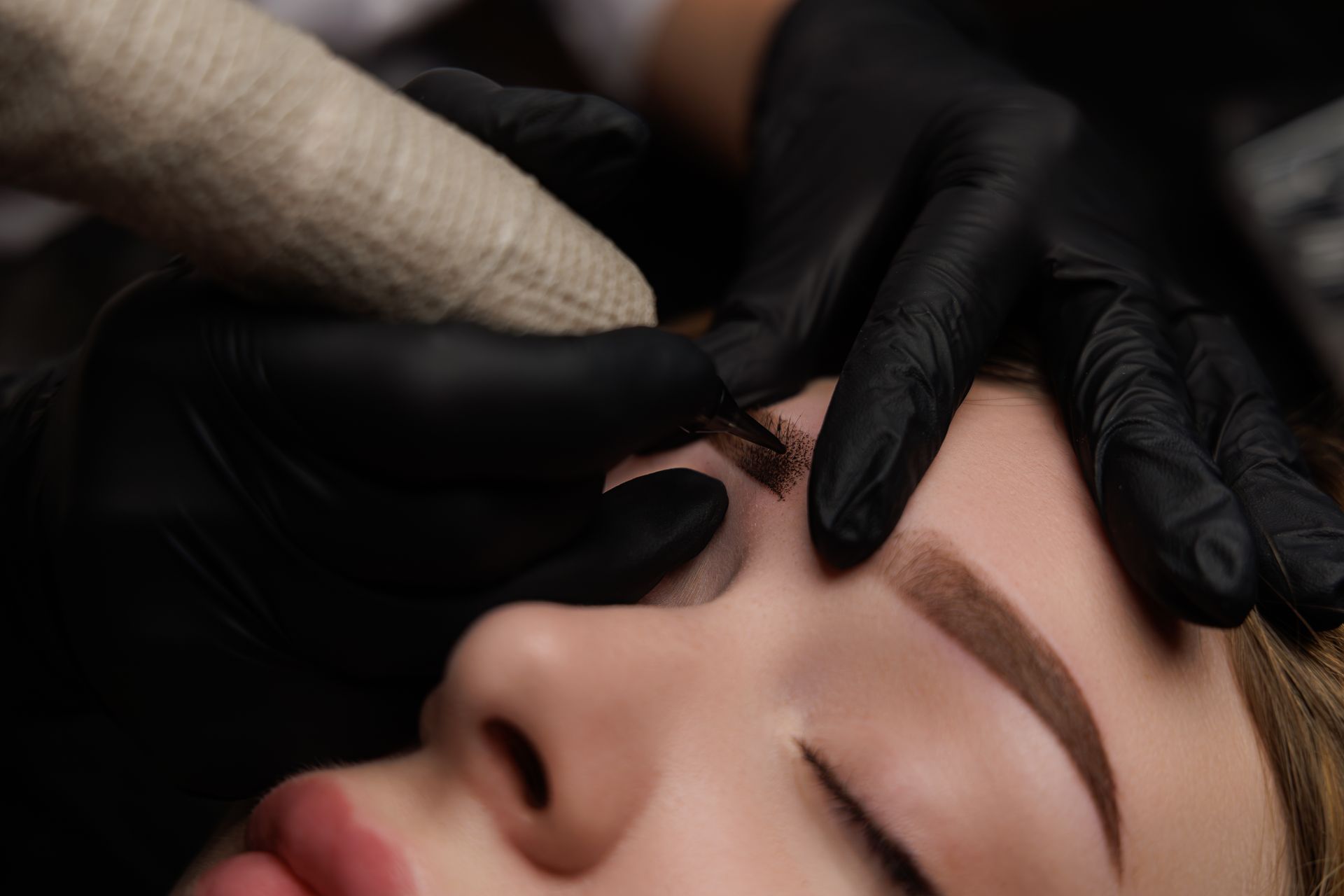 A woman is getting her eyebrows tattooed by a tattoo artist.