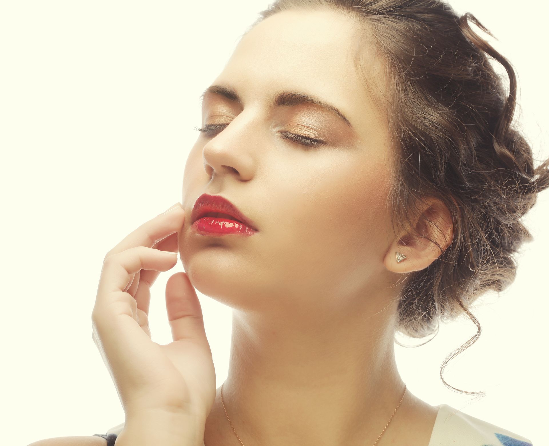 A woman with red lipstick is touching her face with her hand.