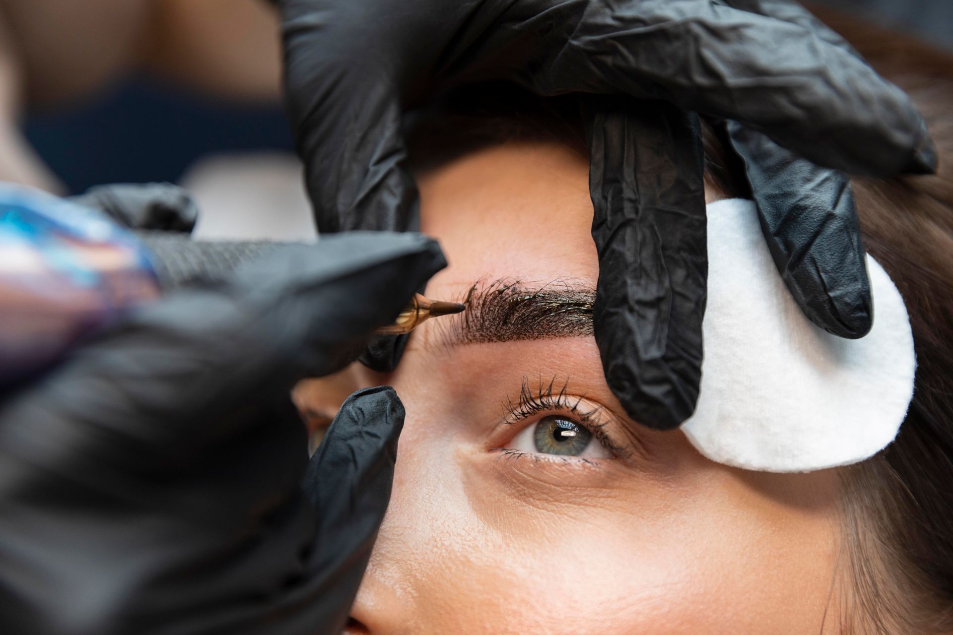 A woman is getting her eyebrows tattooed by a tattoo artist.