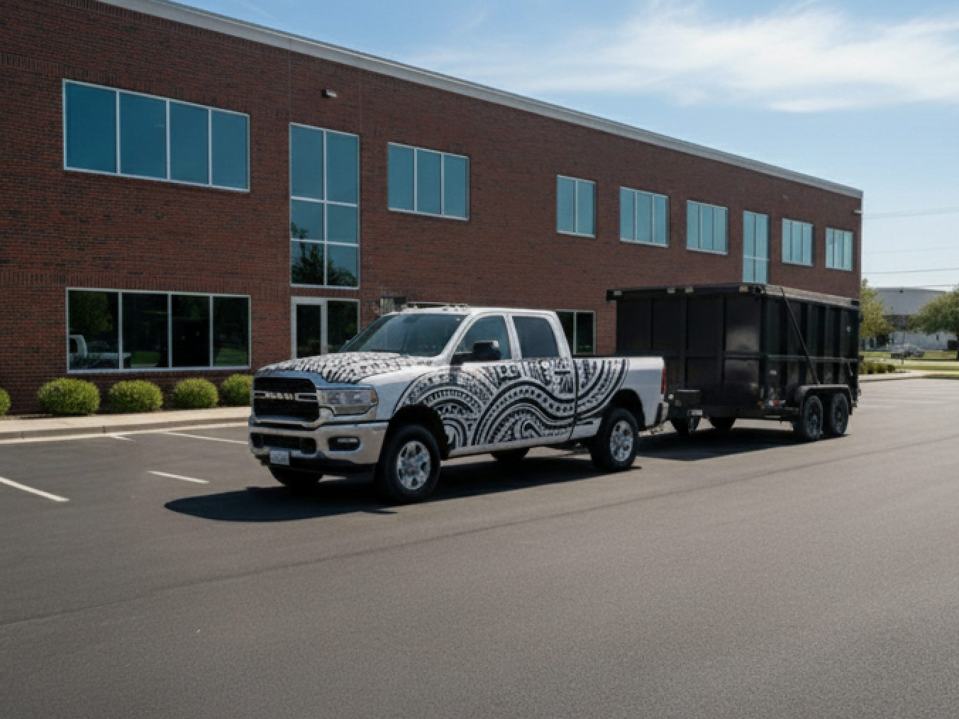 Ram pickup truck with tribal design towing a black trailer in front of a brick building.