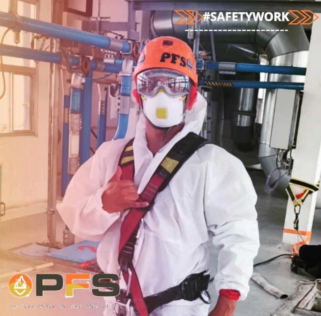 Persona con equipo de protección completo haciendo un gesto de aprobación en un entorno industrial. Lleva casco, gafas protectoras, respirador, traje y arnés de seguridad.