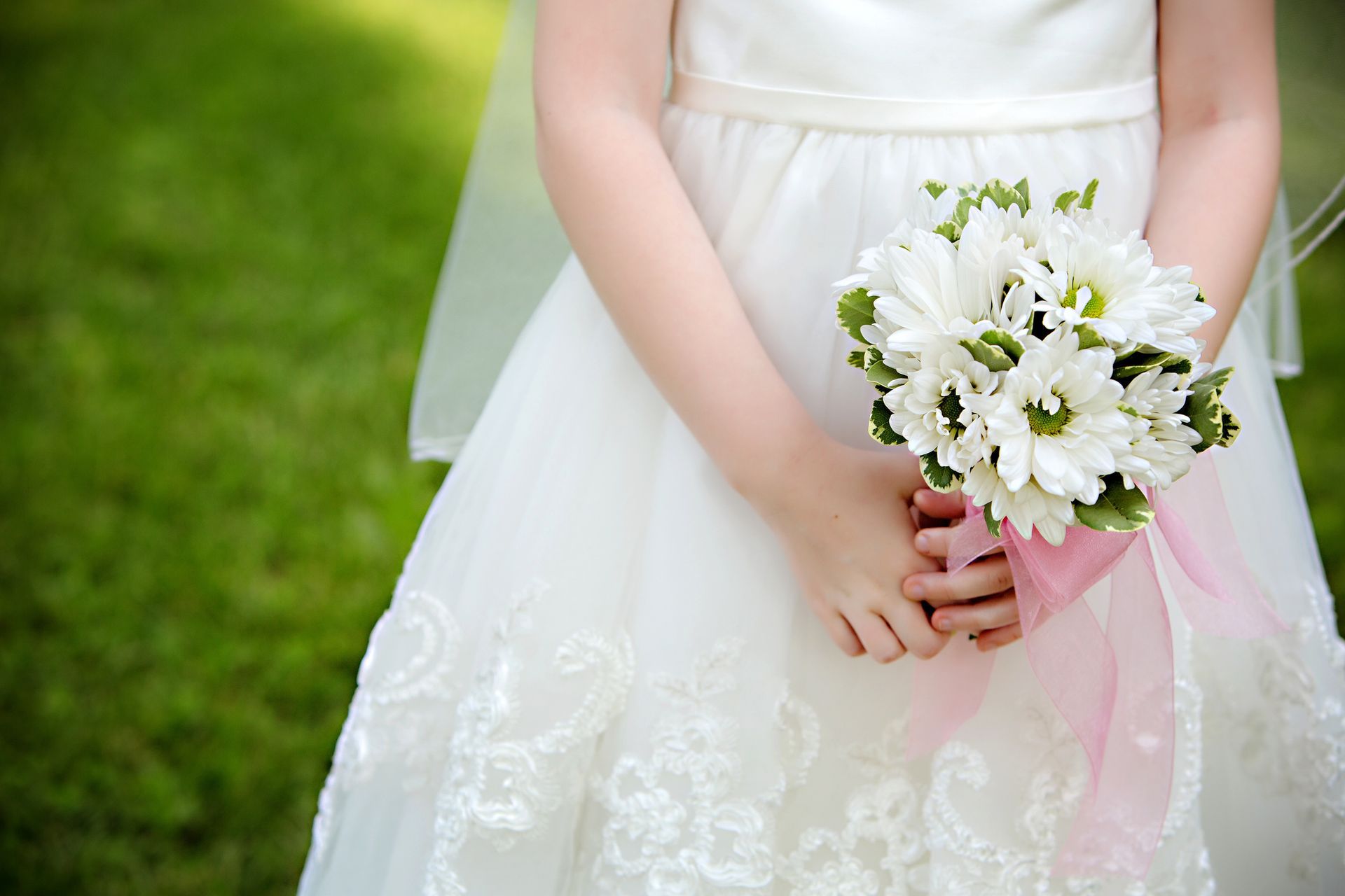 Una damigella in abito bianco tiene in mano un mazzo di margherite bianche.