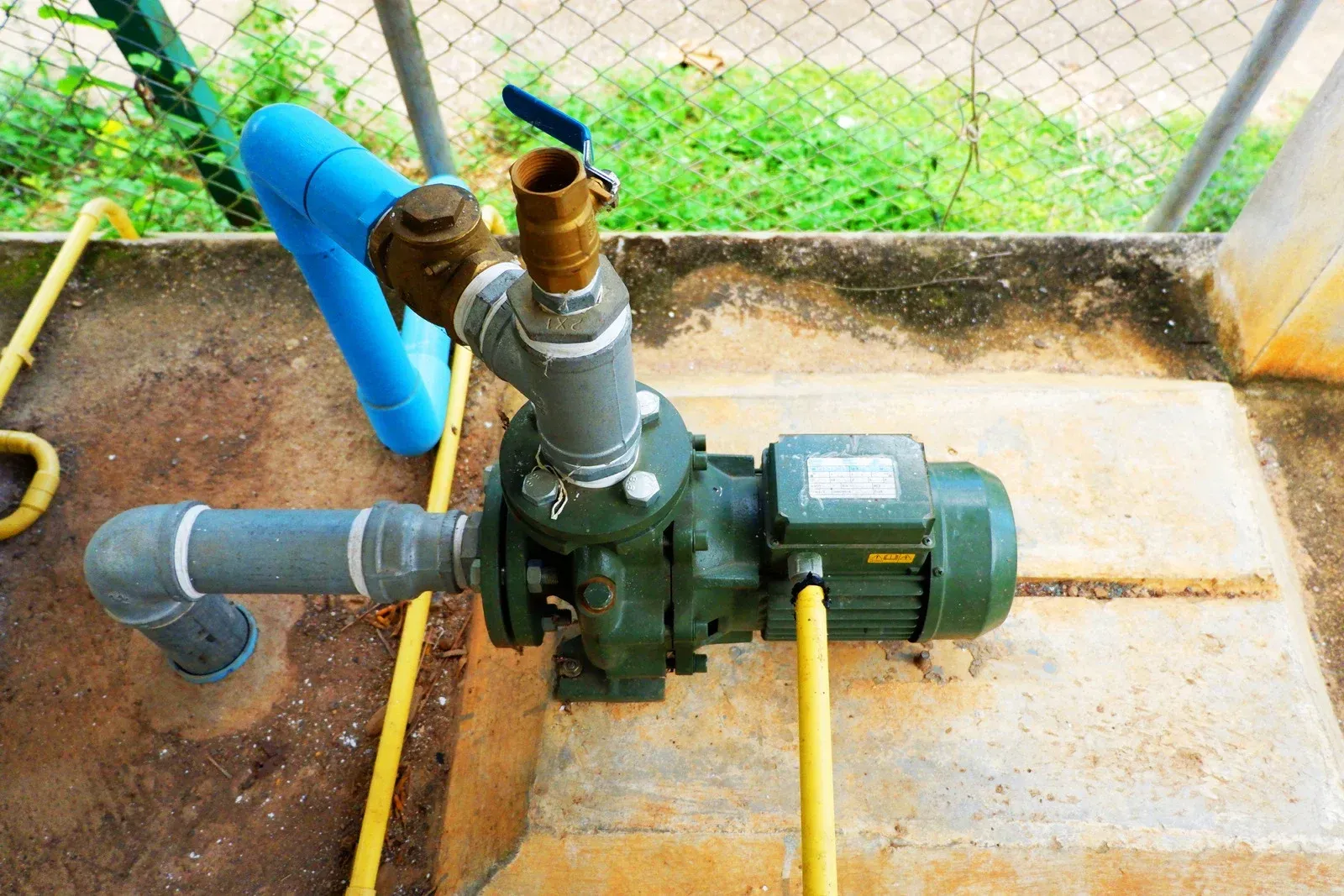 A water pump is sitting on top of a concrete platform next to a fence.