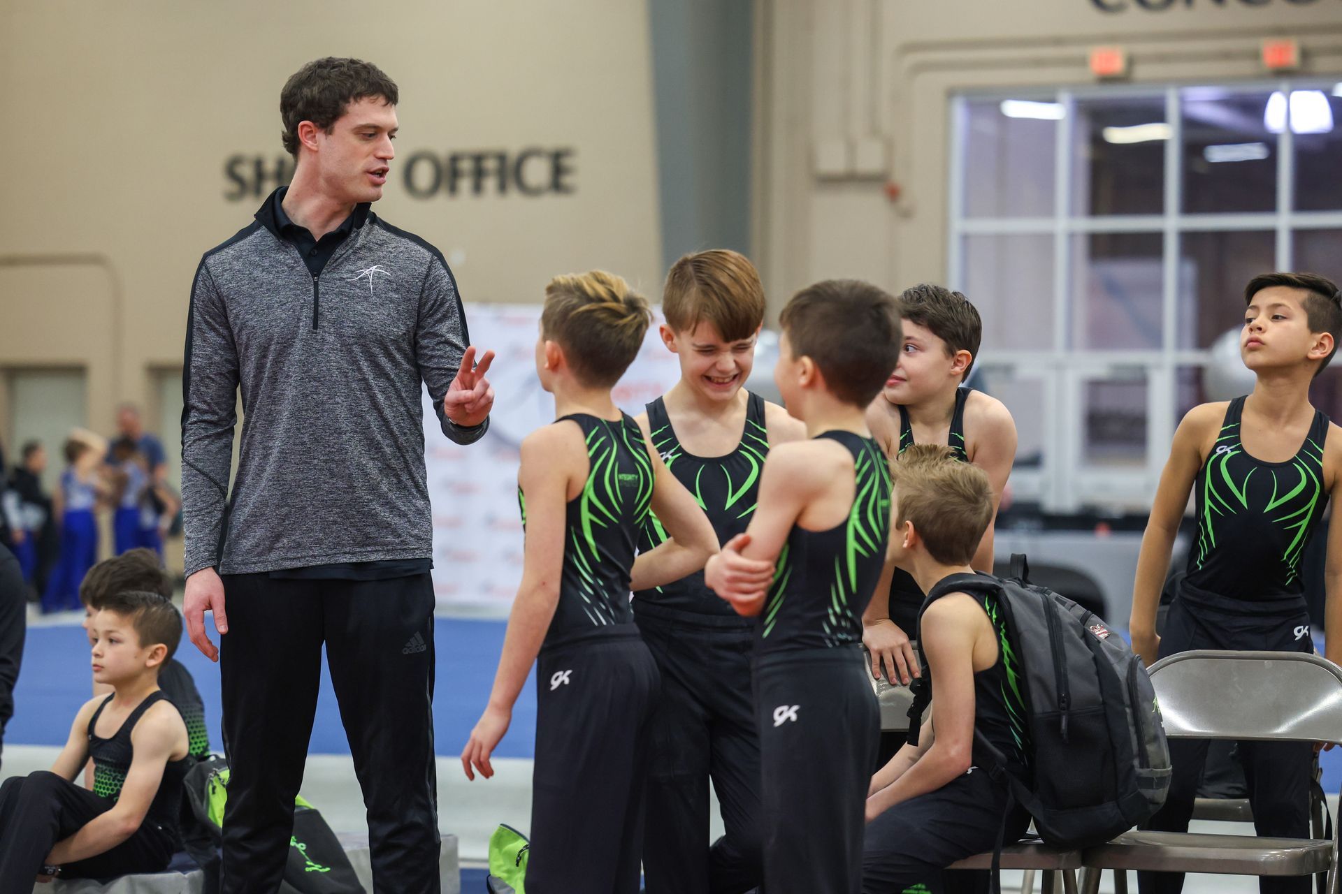 A man is talking to a group of young boys in a gym.