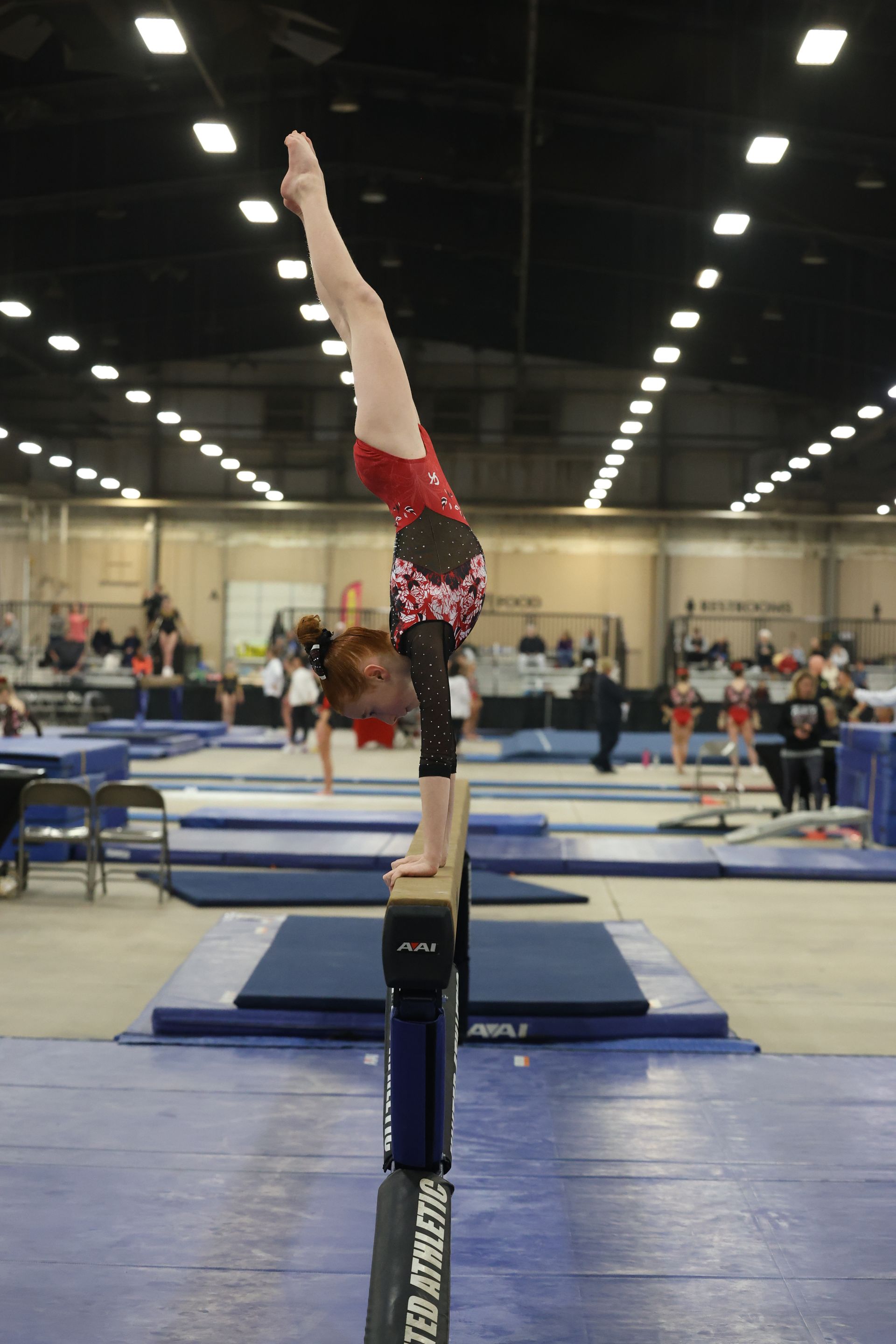 A girl is doing a handstand on a balance beam in a gym