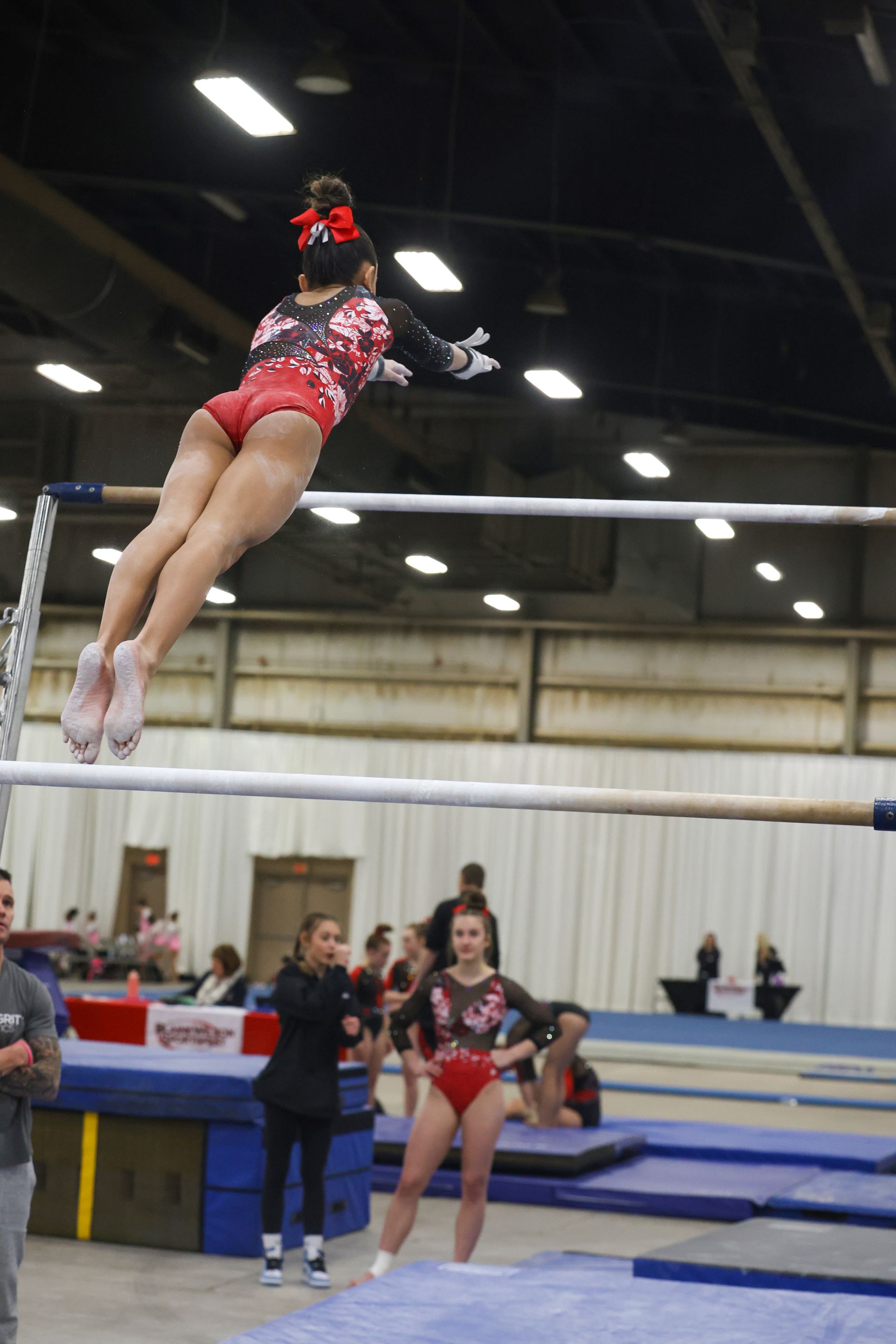 A female gymnast is jumping over a bar in a gym