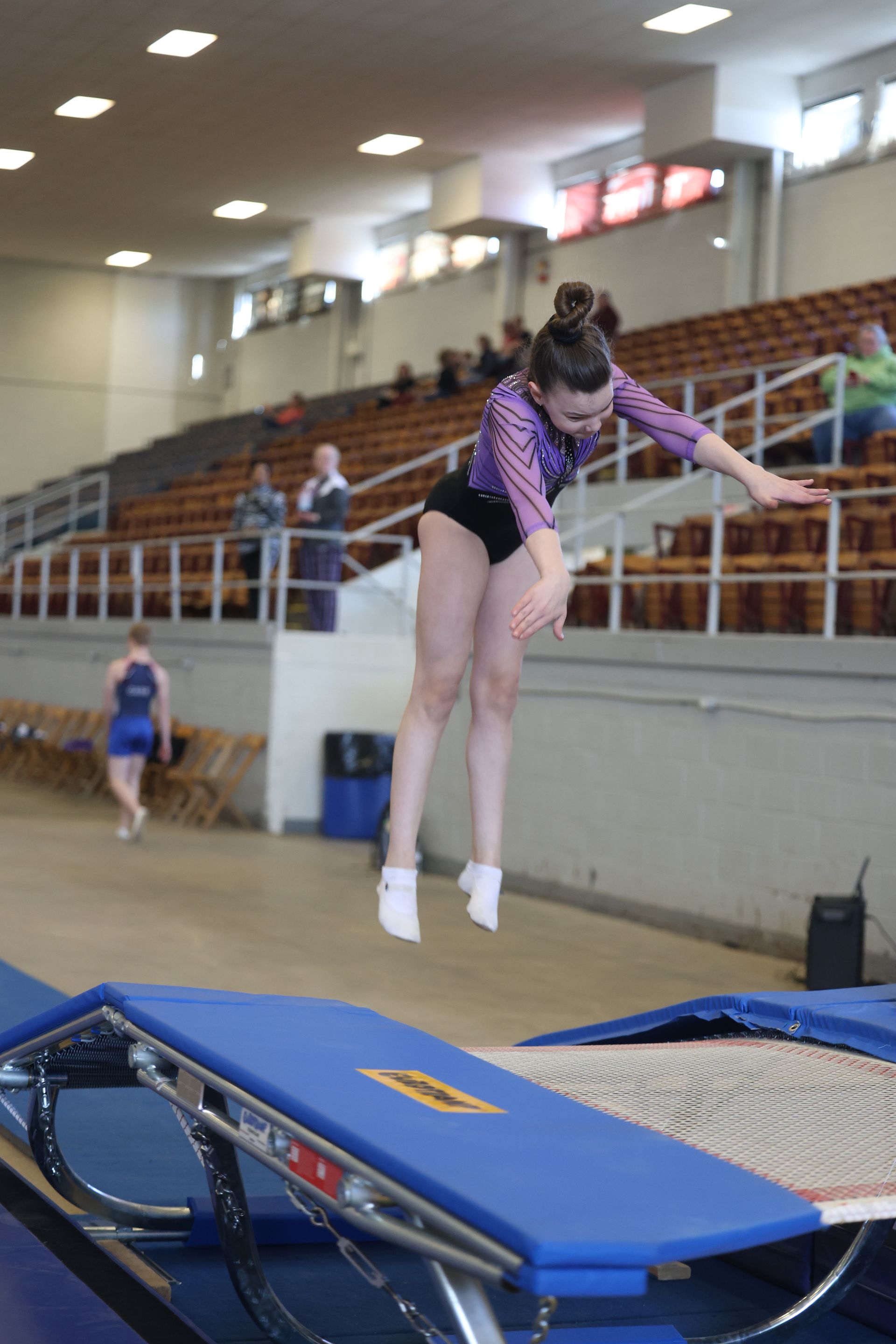 A girl is jumping on a trampoline in a gym.