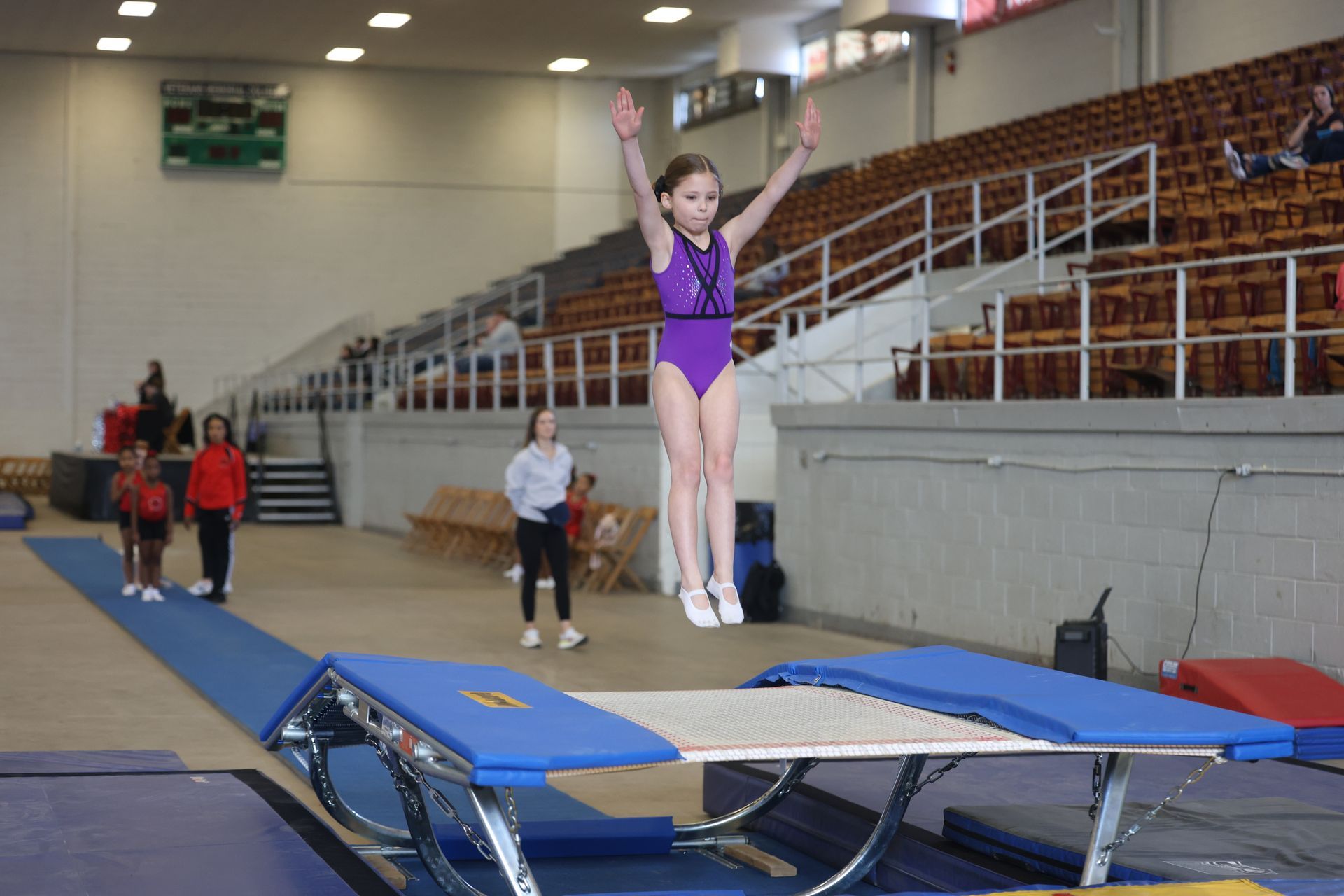 A young girl is jumping on a trampoline in a gym.