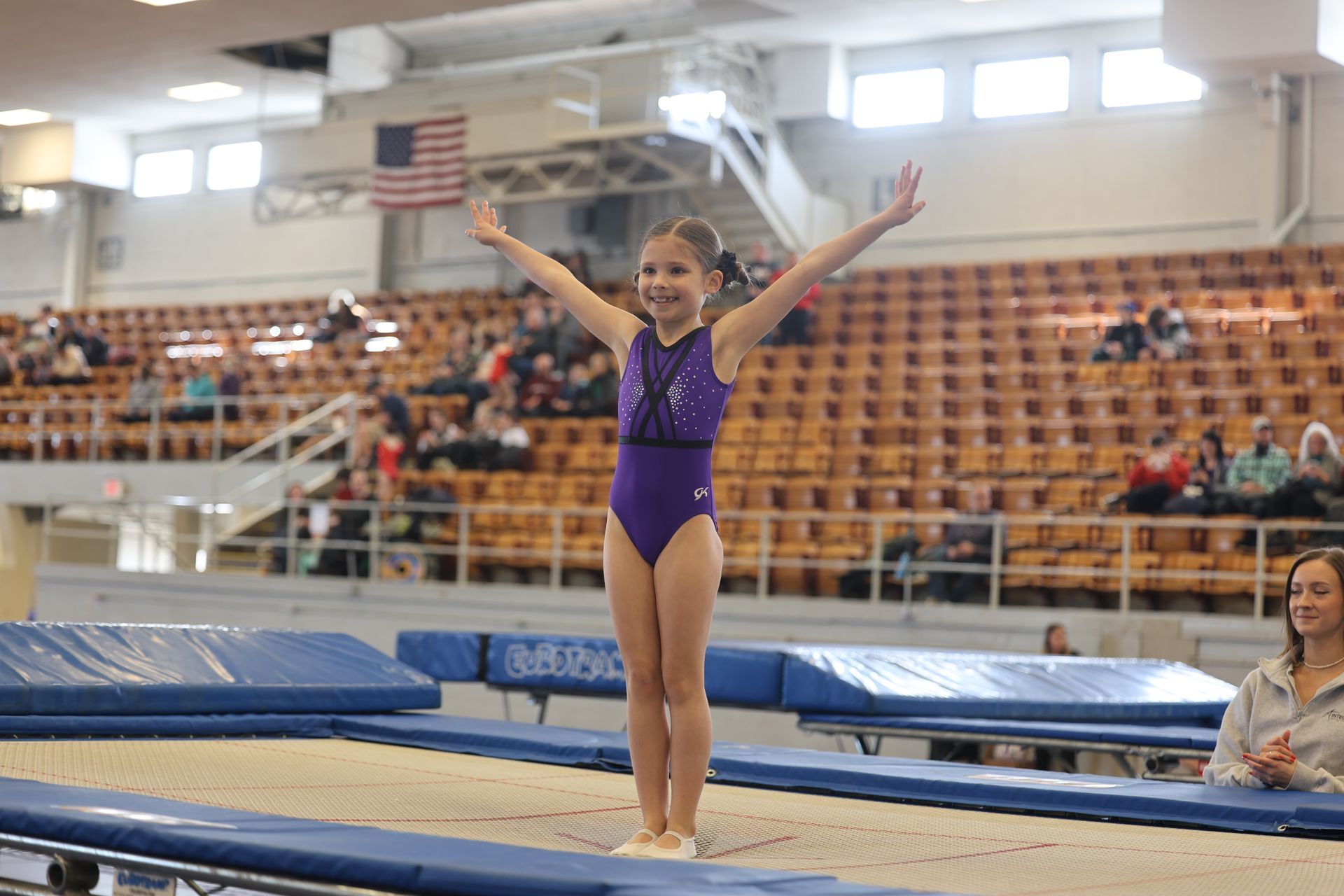 A young girl is standing on a trampoline with her arms outstretched.