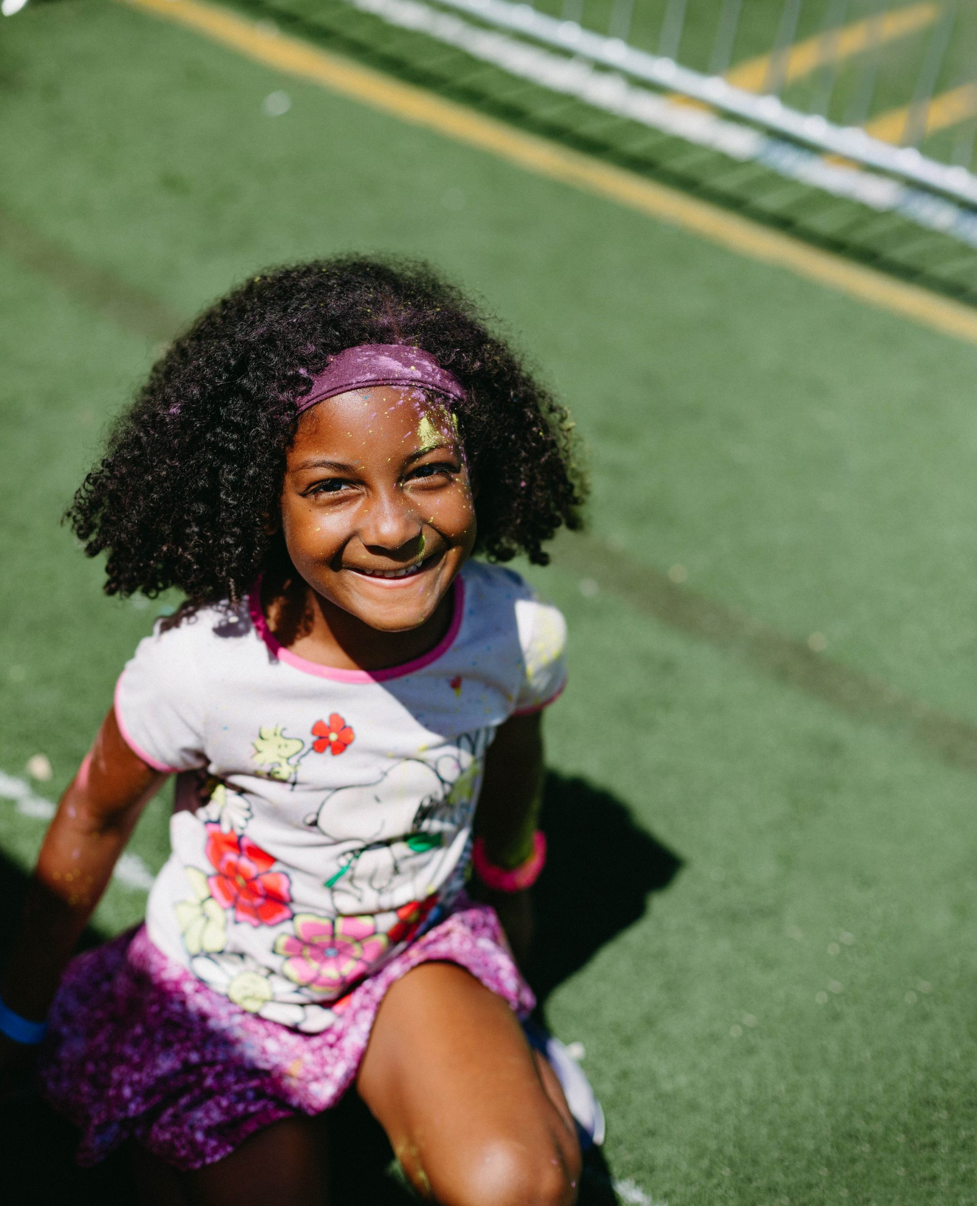 A little girl is sitting on the grass and smiling at the camera.