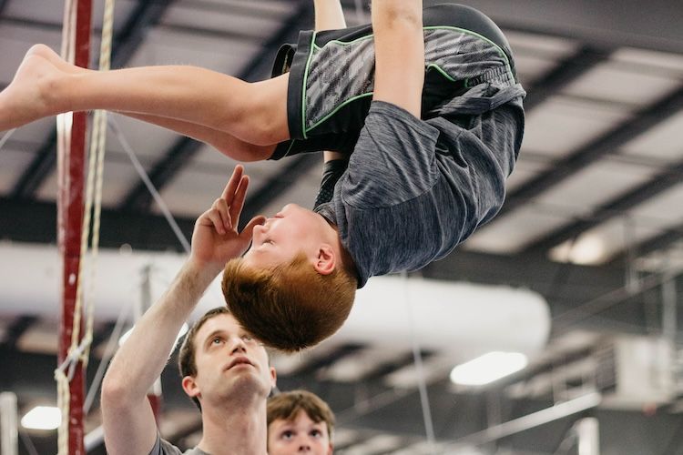 A young boy is doing a handstand on a gymnastics bar.