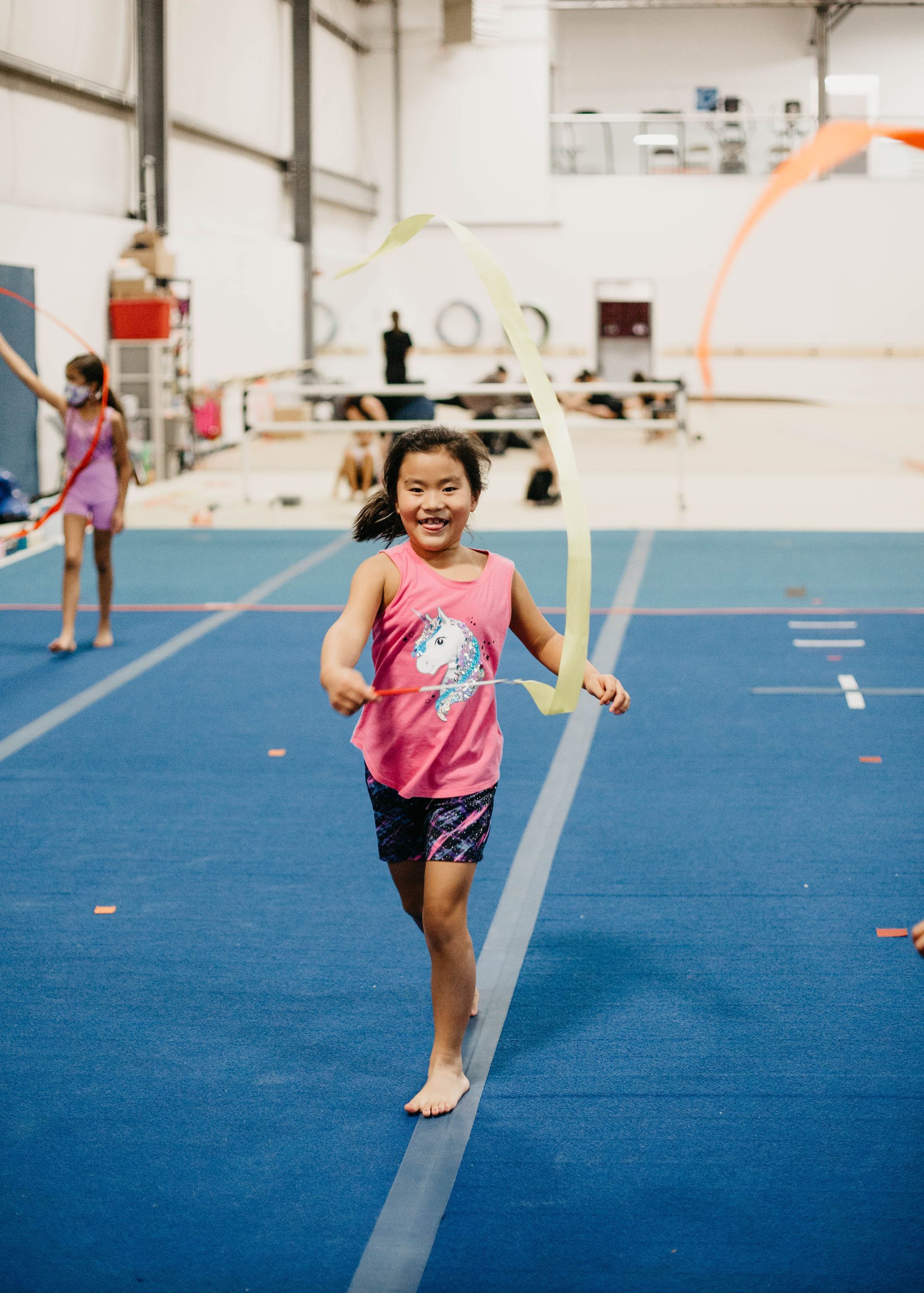 A little girl is playing with a ribbon on a gym floor.