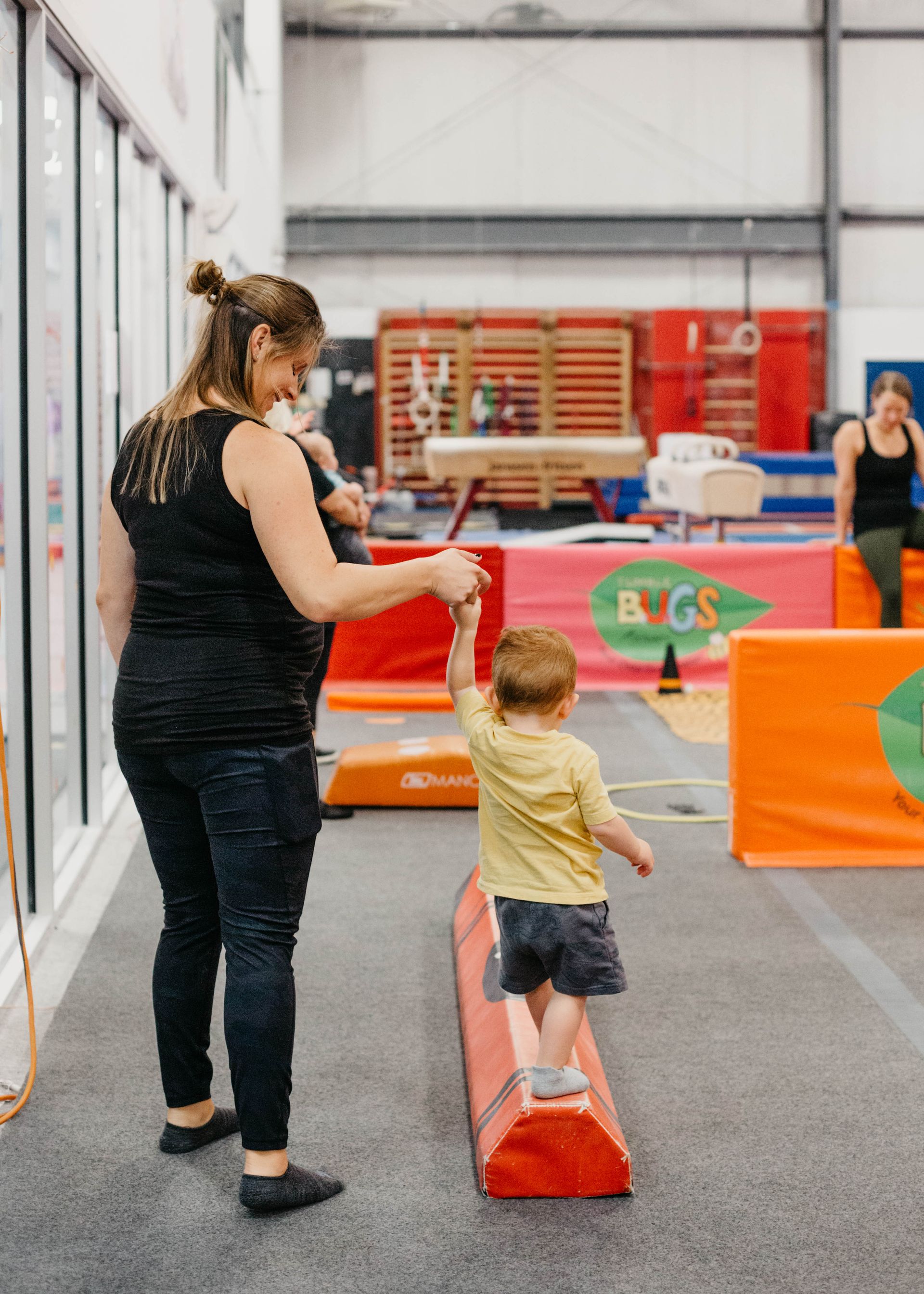 A woman is helping a little boy balance on a balance beam.