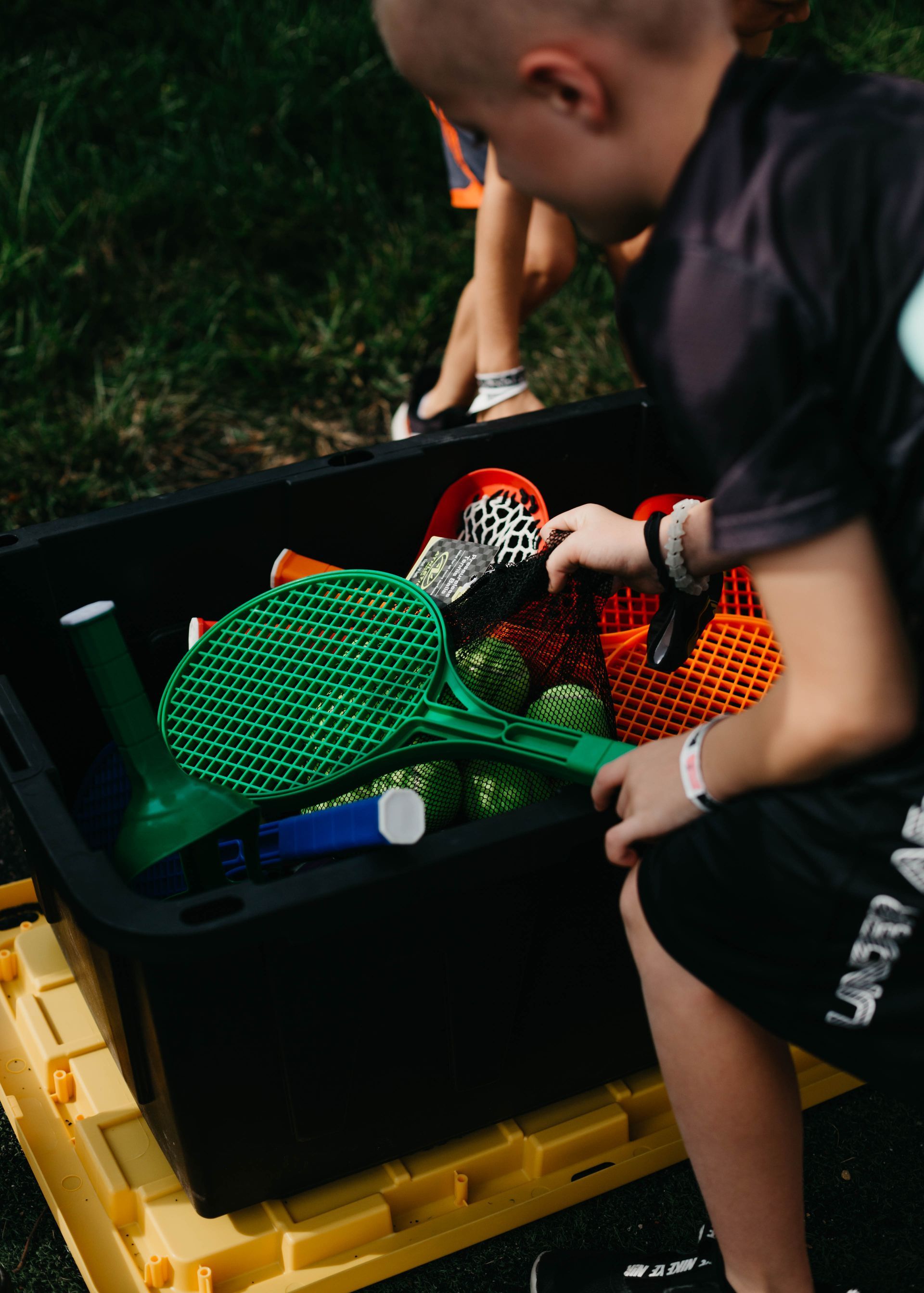 A young boy is kneeling down next to a black bin filled with toys.