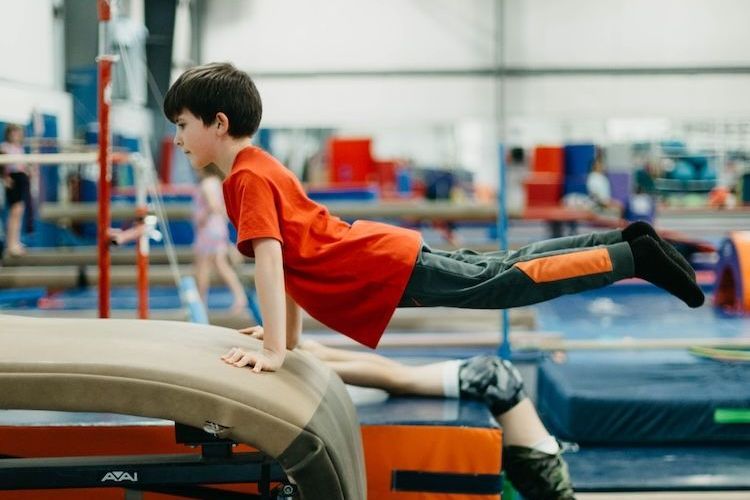 A young boy is doing a trick on a balance beam in a gym.