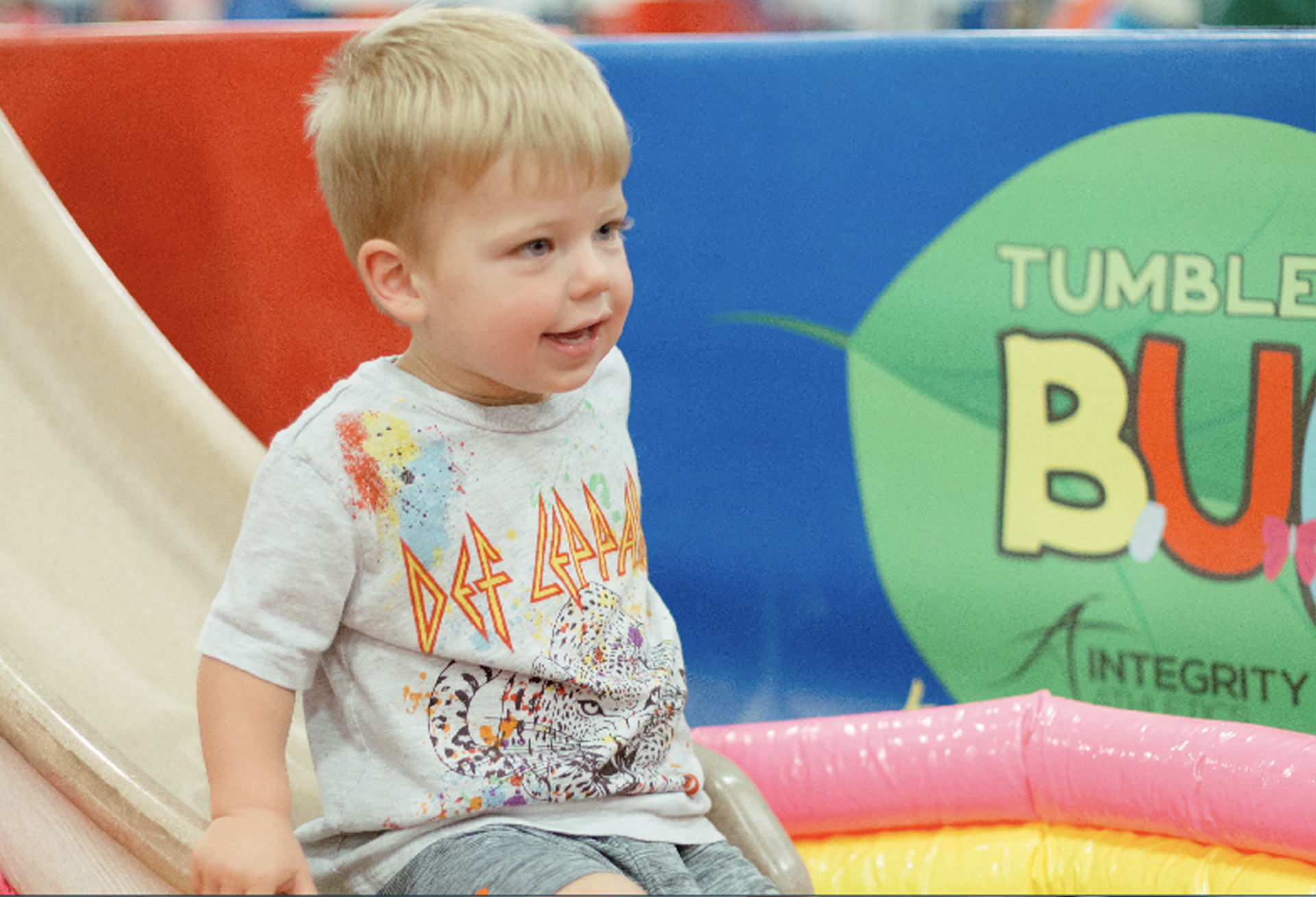 A little boy is sitting on a slide in front of a banner that says tumble bubble