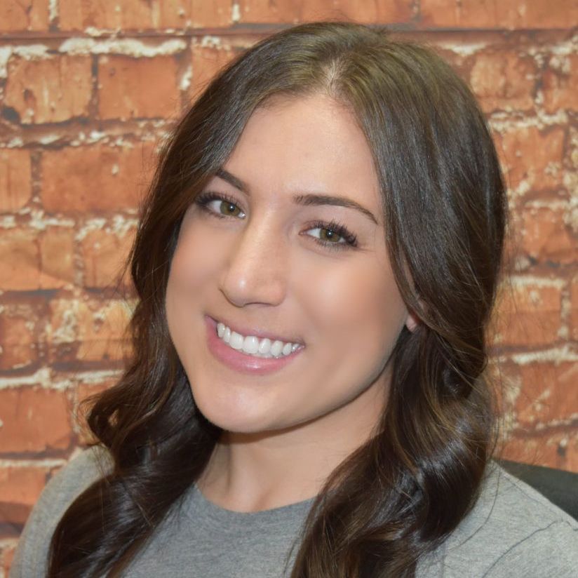 A woman is smiling in front of a brick wall.