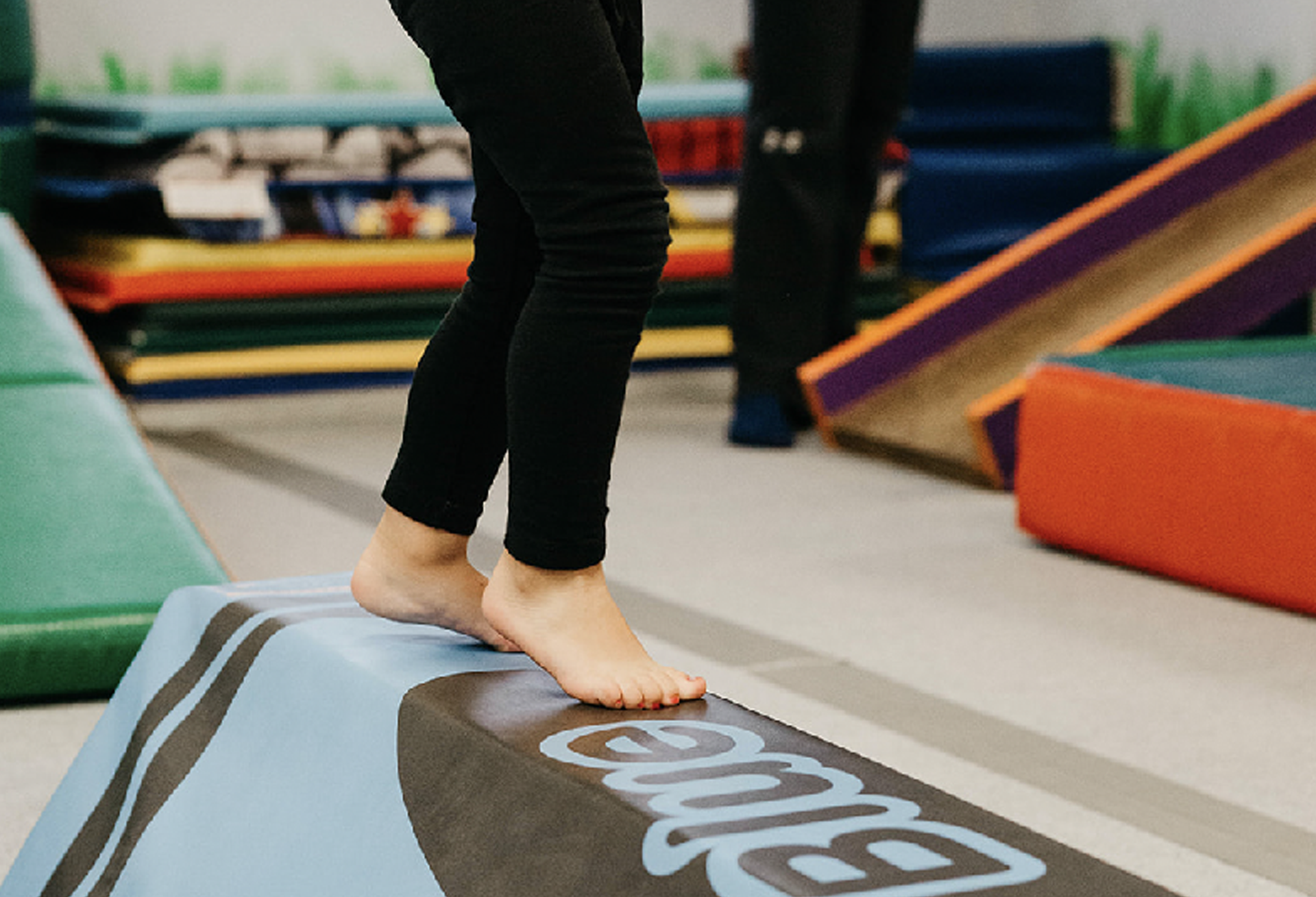 A child is standing on a balance beam in a gym.