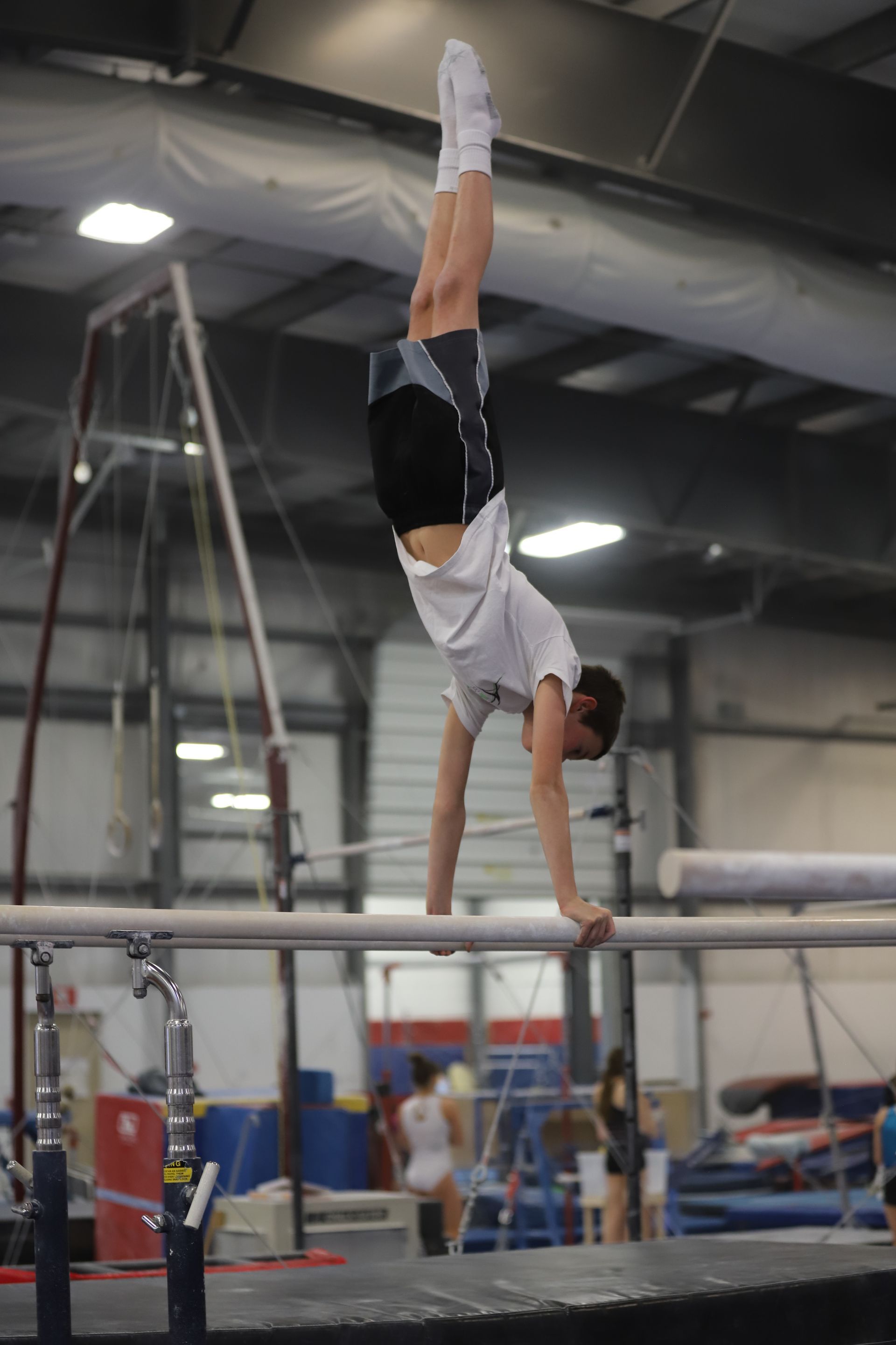 A man is doing a handstand on a parallel bars in a gym.