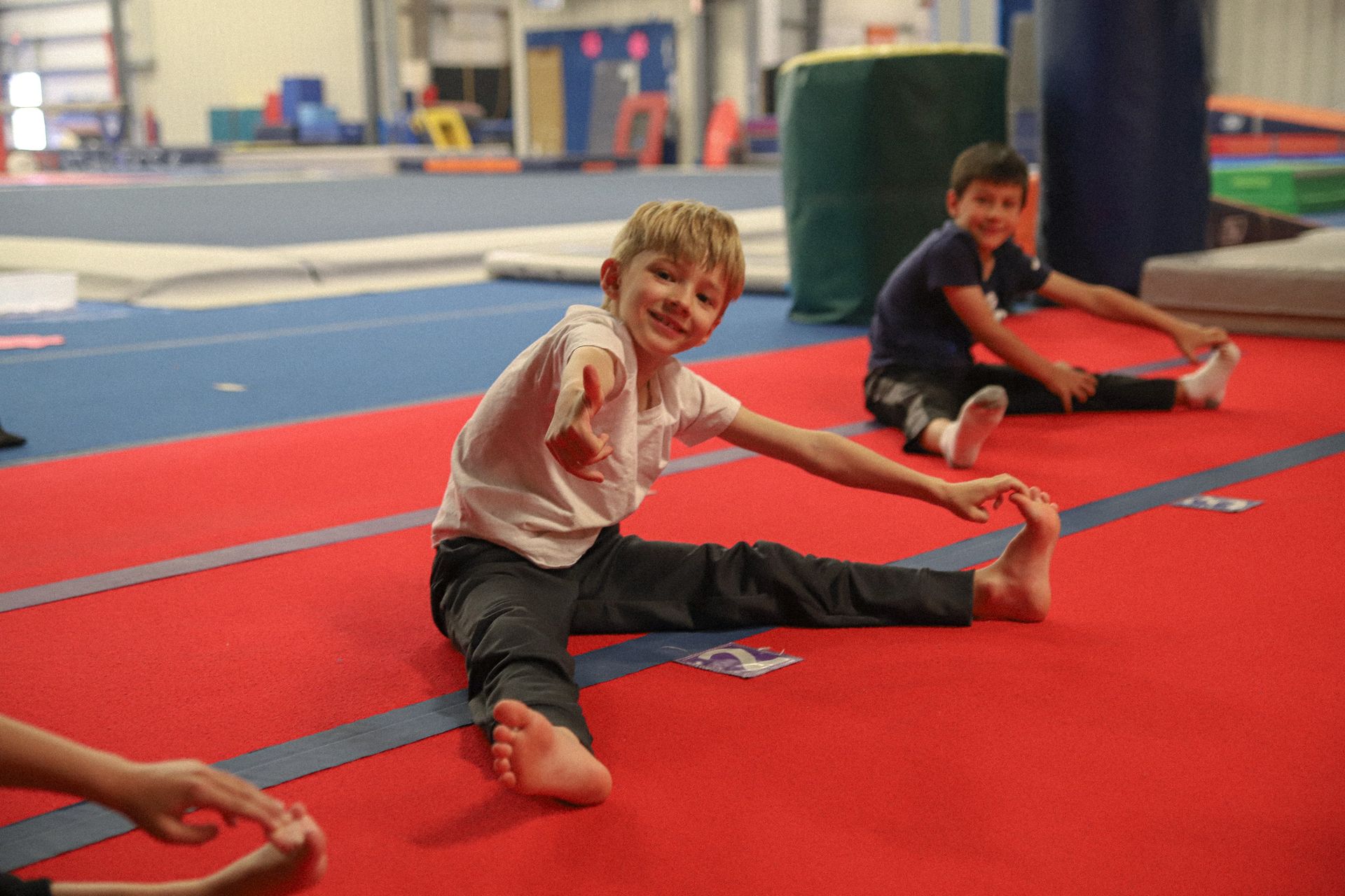 A young boy is sitting on the floor stretching his legs.