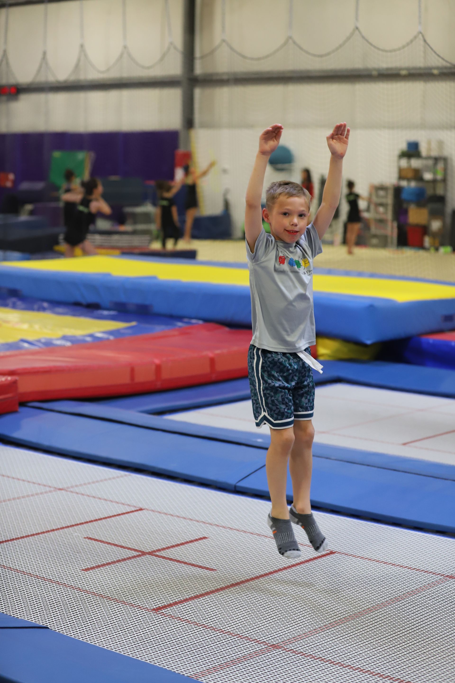 A young boy is jumping on a trampoline in a gym.
