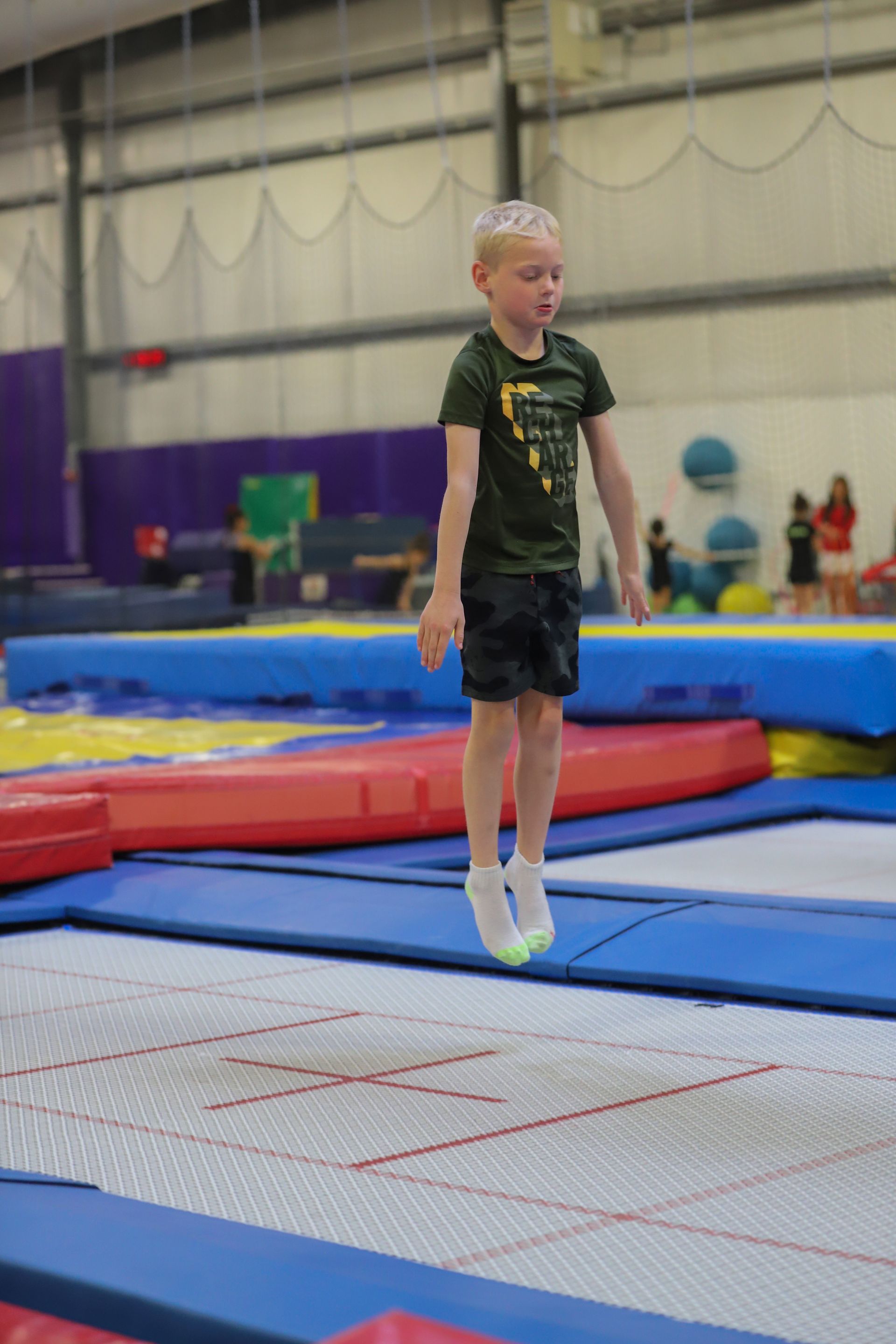 A young boy is jumping on a trampoline in a gym.